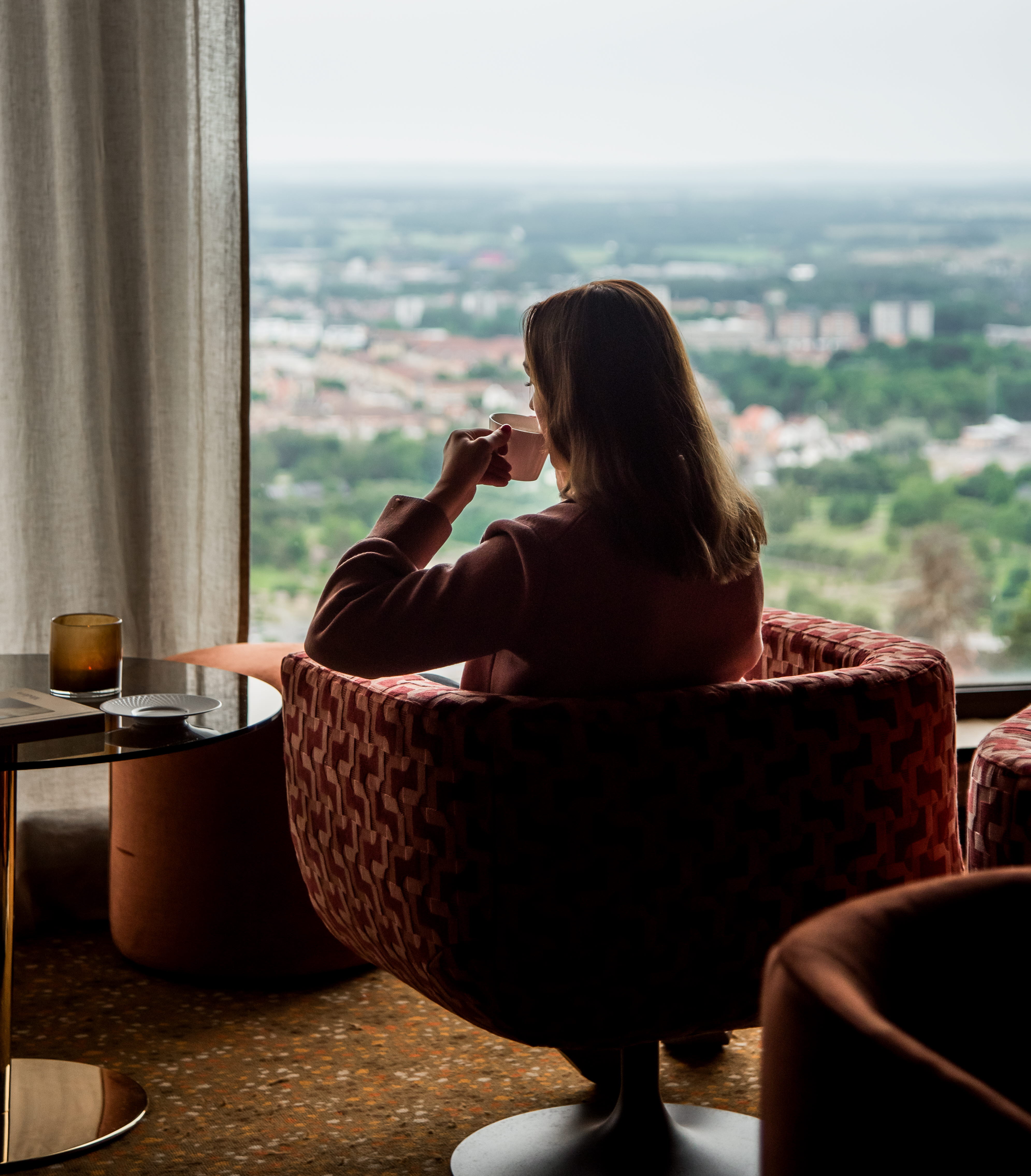 Kvinna som sitter i en fåtölj och kikar ut genom ett fönster.