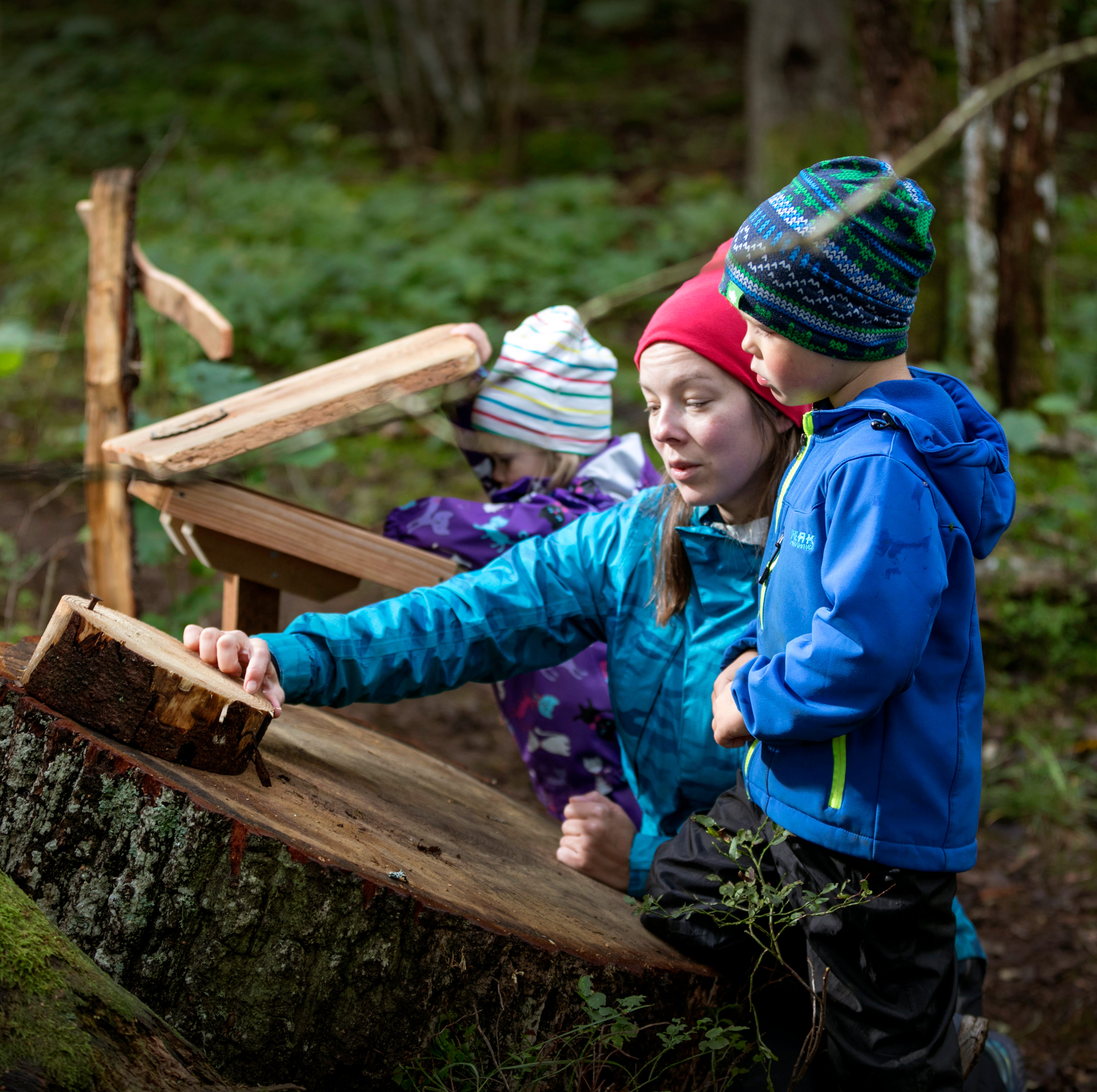 En kvinna med två barn utforskar stockar i naturen.