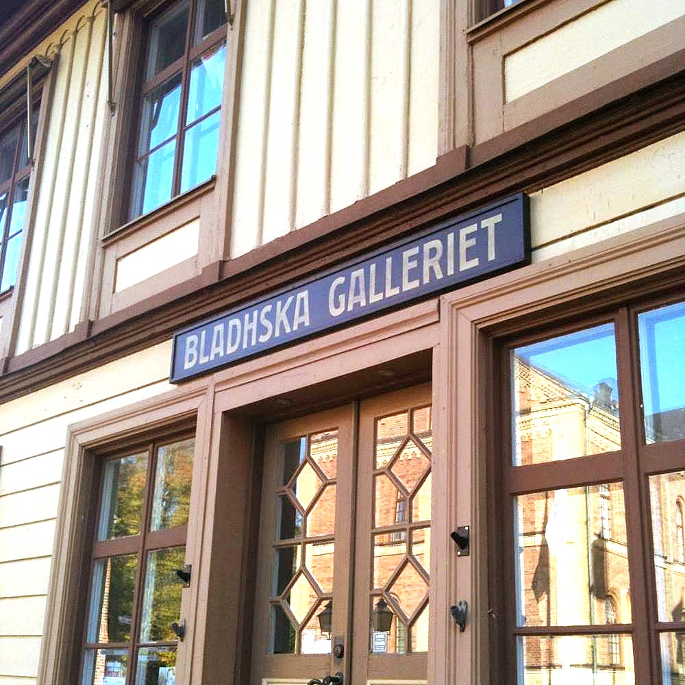 Ett gult trähus med en skylt över dörren som det står Bladhska galleriet på.