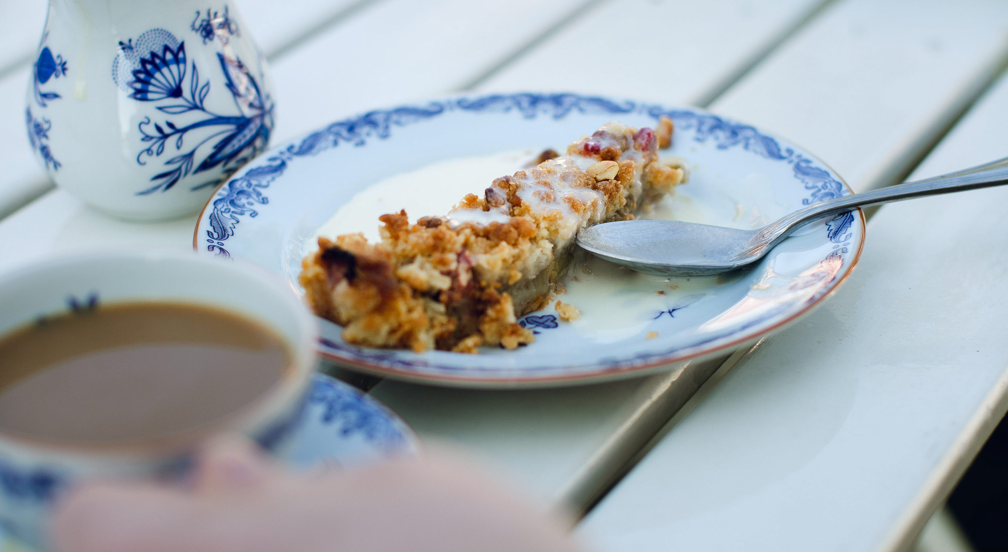 Vita tallrikar med blå mönstrad kant. En bit äpplekaka med vaniljsås och en kaffekopp.
