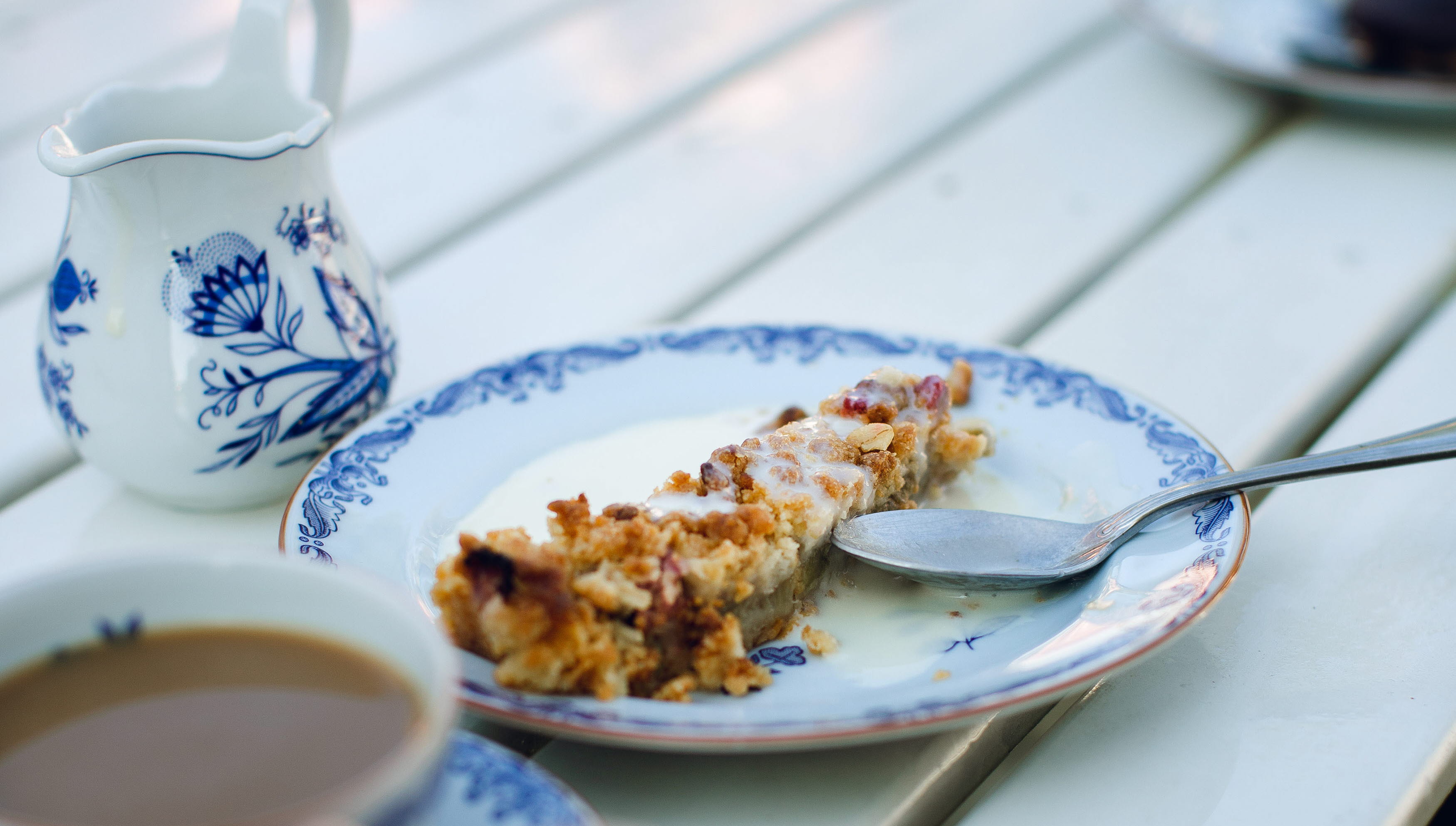 Vita tallrikar med blå mönstrad kant. En bit äpplekaka med vaniljsås och en kaffekopp.