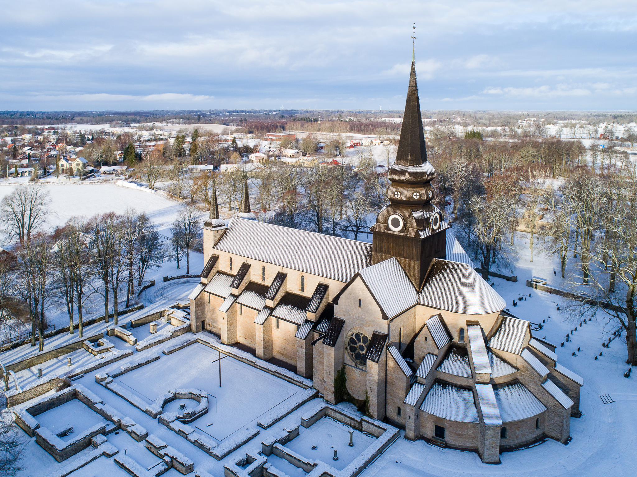 Drönarbild över Varnhems klosterkyrka med snö på taket och det omkringliggande landskapet.