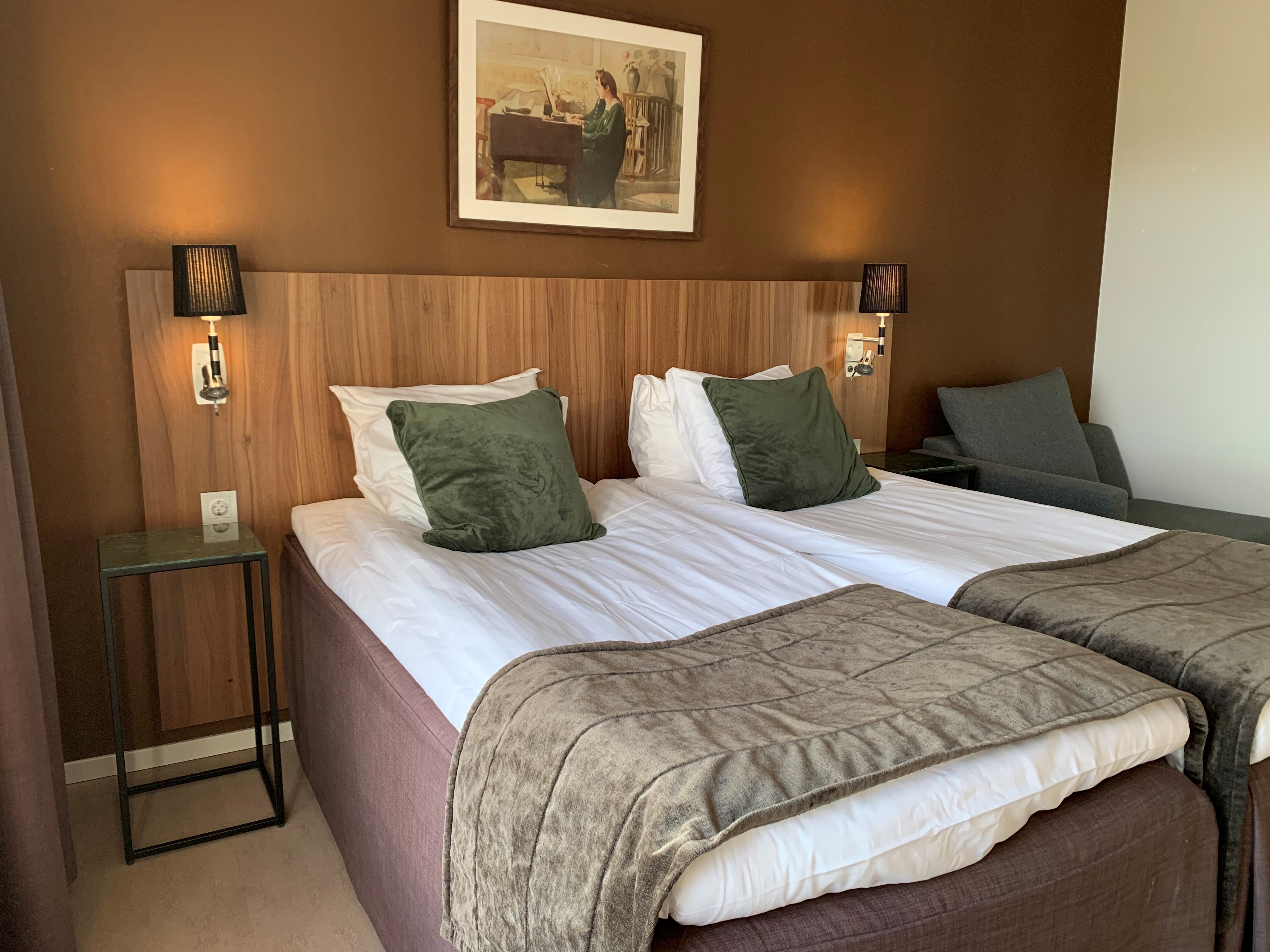 en dubbelsäng med bruna filtar på och en brun vägg bakom.