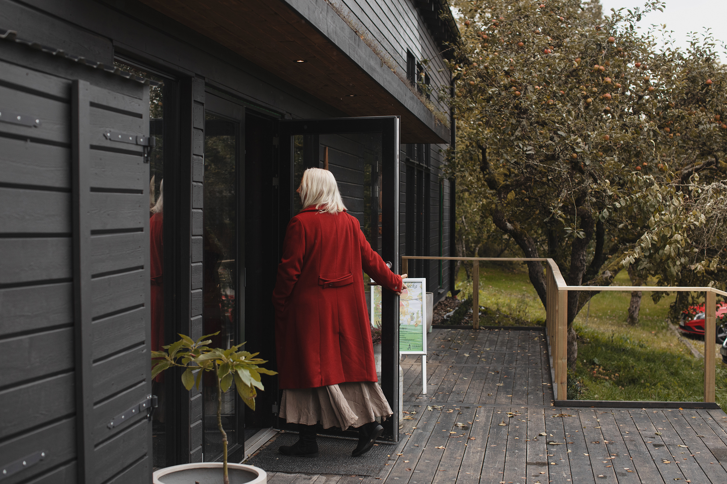 Kvinna i röd kappa går in i ett svart trähus.