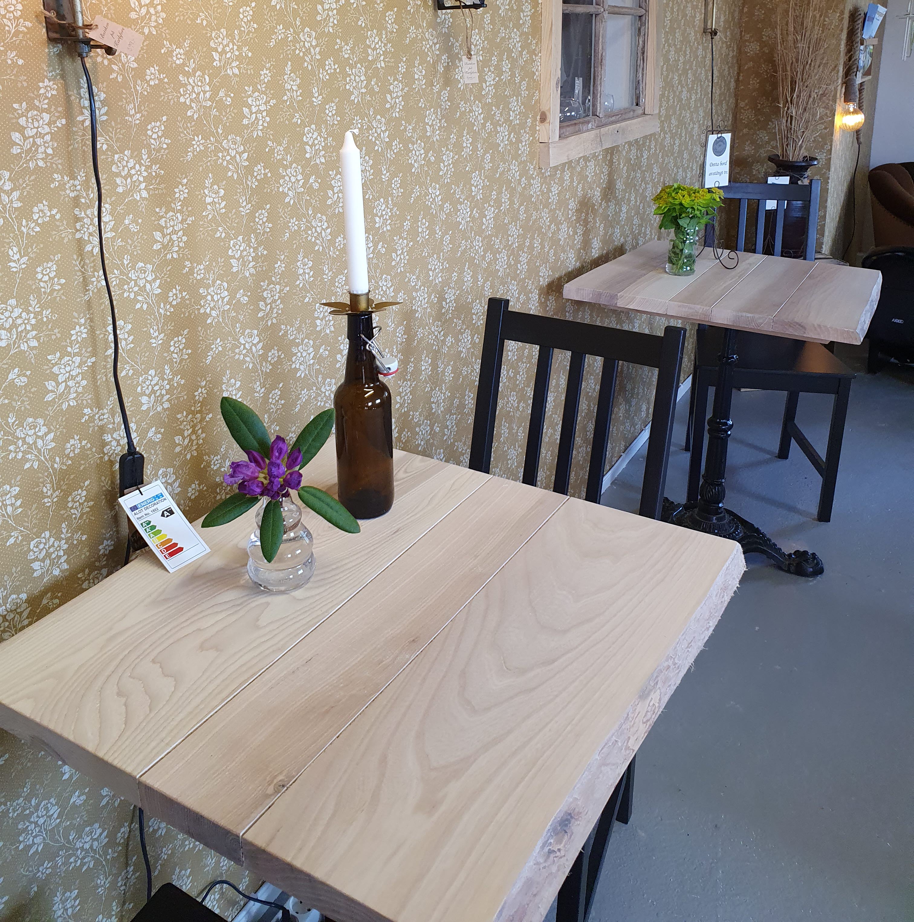 Två träbord med svarta stolar. Vasar med blommor på borden och en ljusstake.