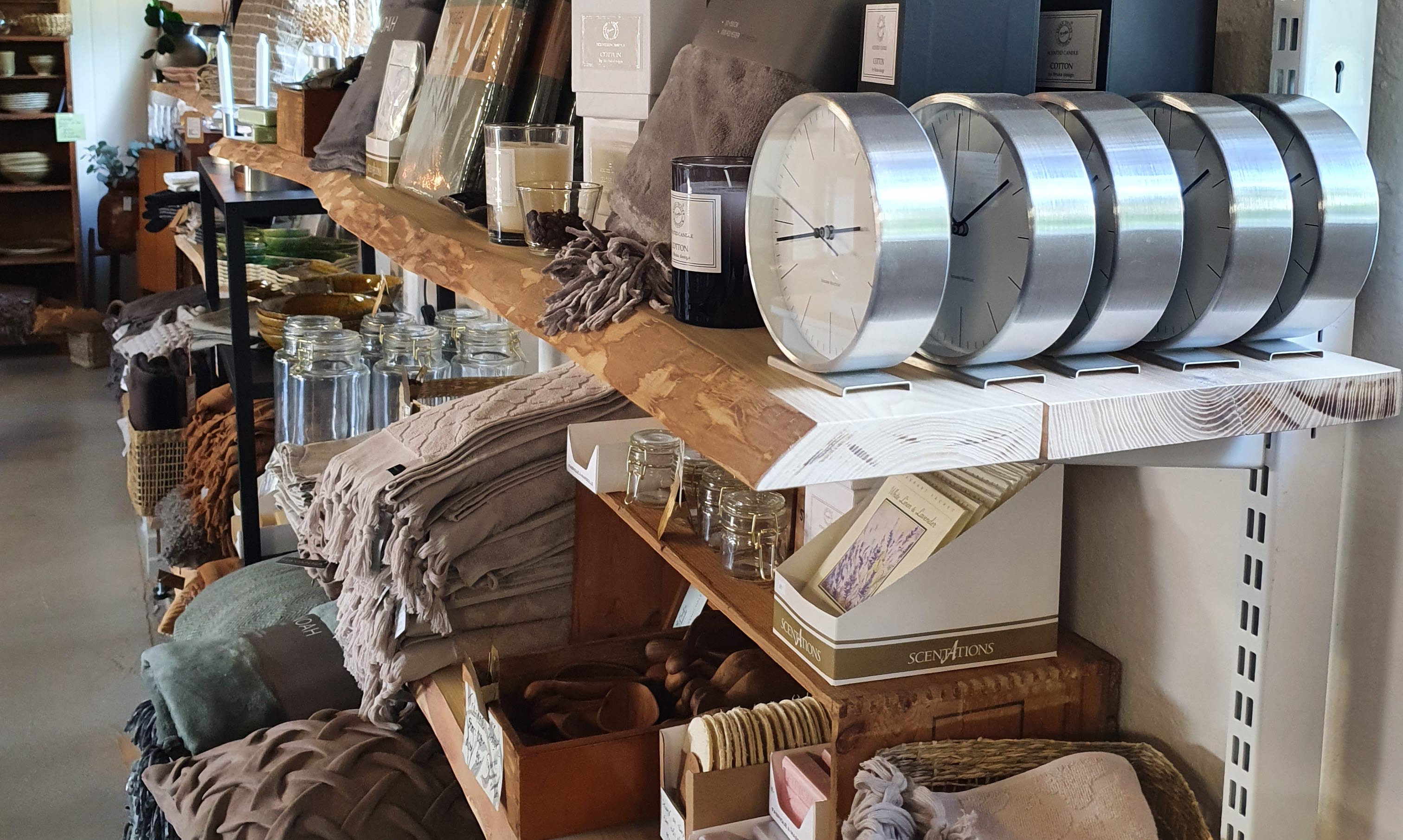 Tre hyllor i trä med olika inredningsprylar på t ex. kuddar och ljuslyktor.