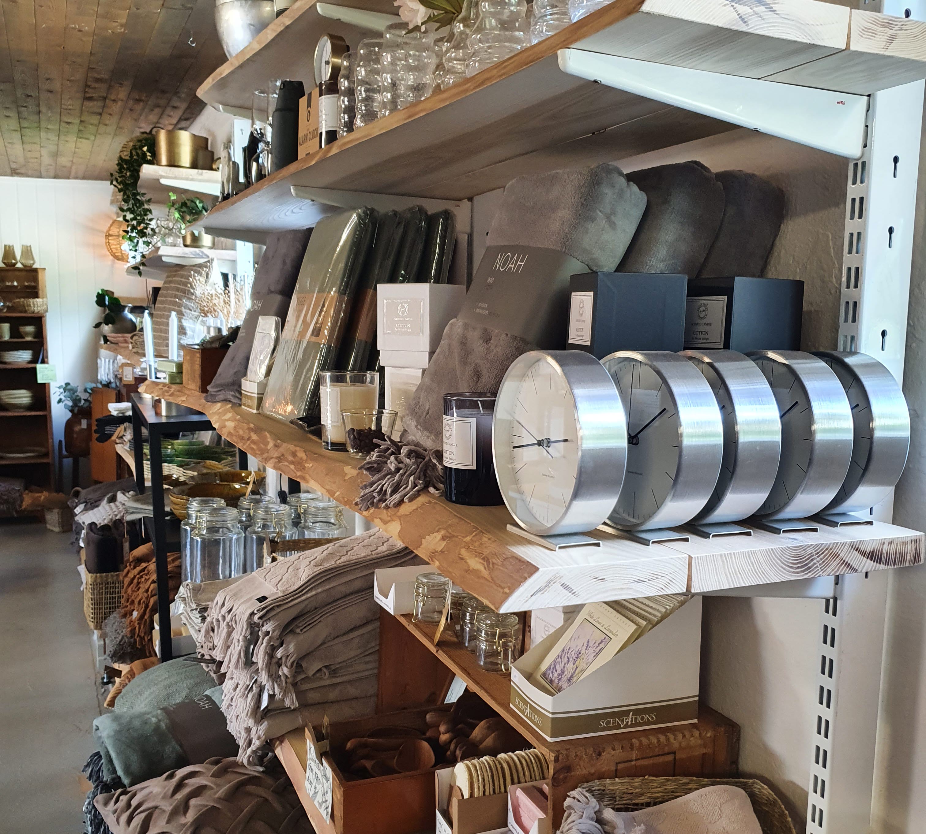 Tre hyllor i trä med olika inredningsprylar på t ex. kuddar och ljuslyktor.