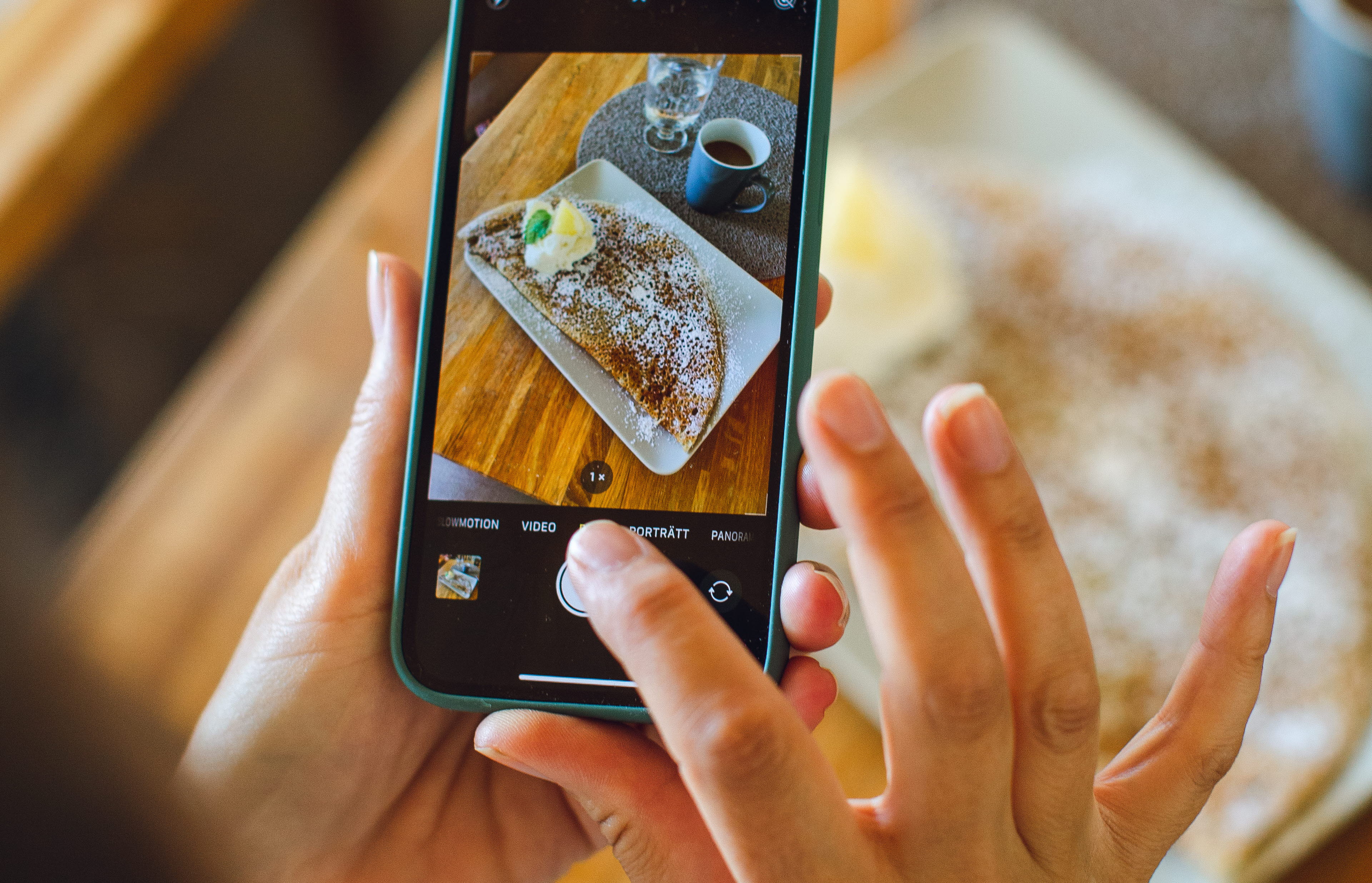 En person tar en bild med en smartphone. I telefonen syns bilden som är på en galette och en kopp kaffe. 
