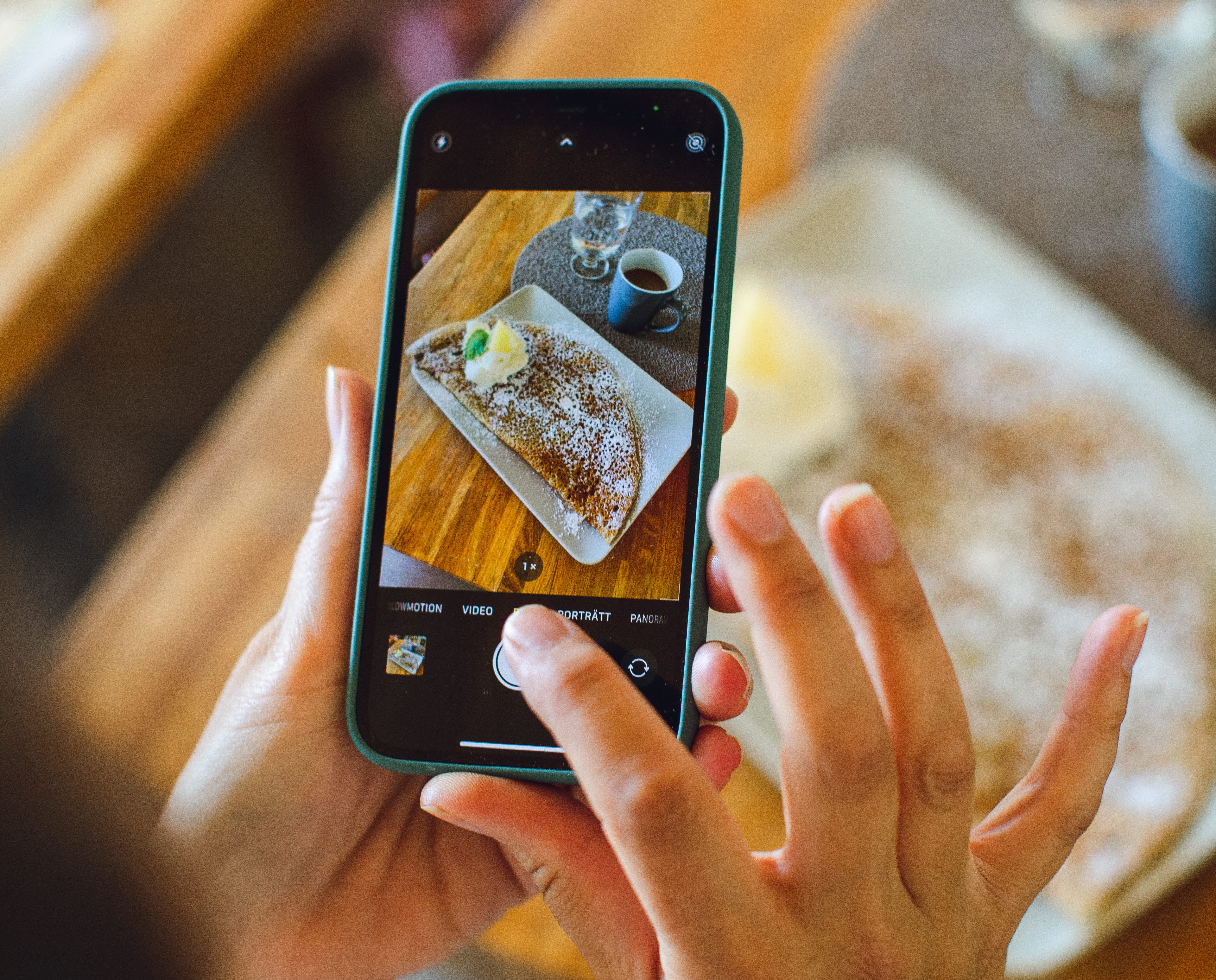 En person tar en bild med en smartphone. I telefonen syns bilden som är på en galette och en kopp kaffe. 