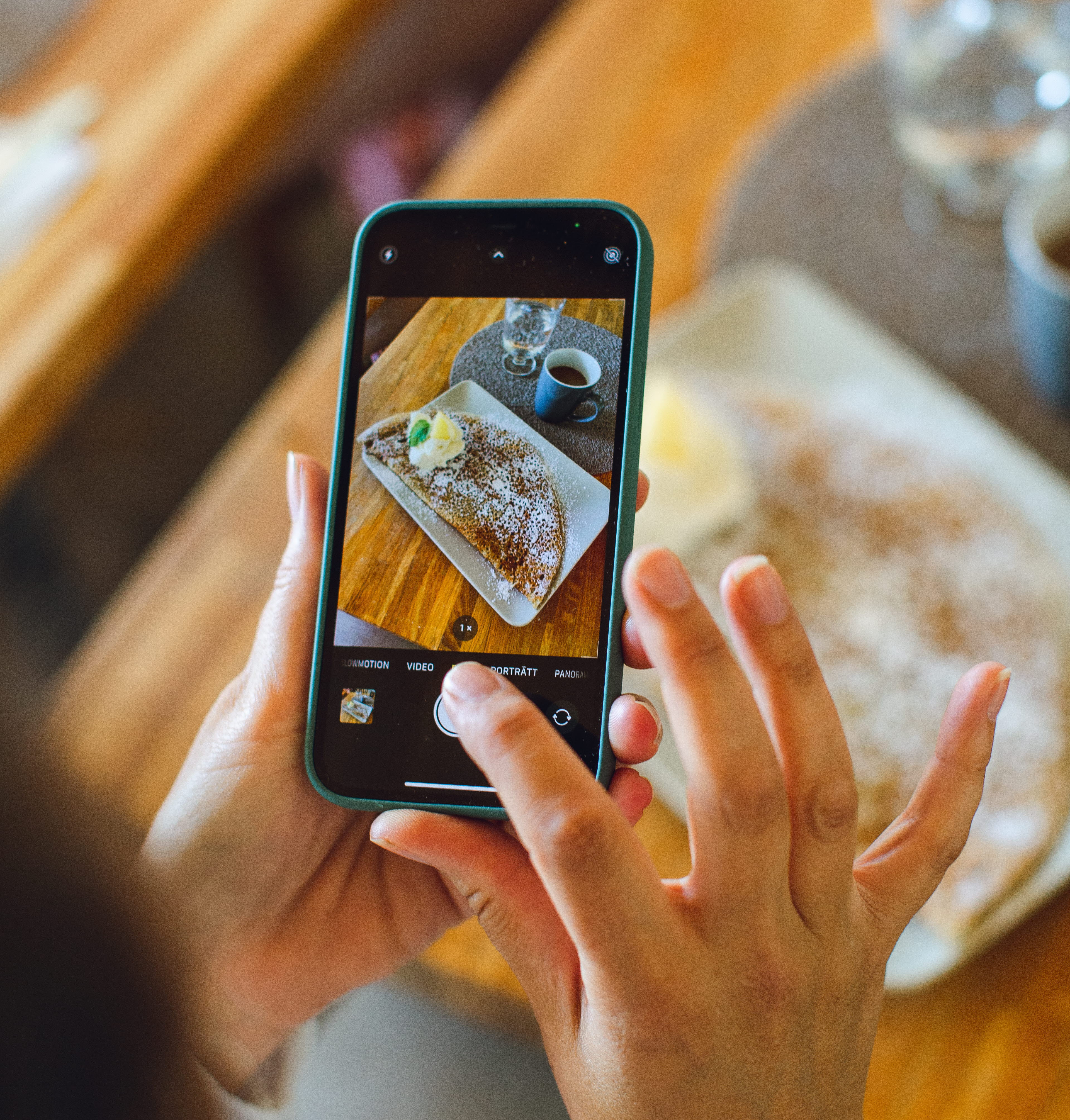 A person is taking a picture with a smartphone. In the phone you can see the picture which is a picture of a crêpe and a cup of coffee.