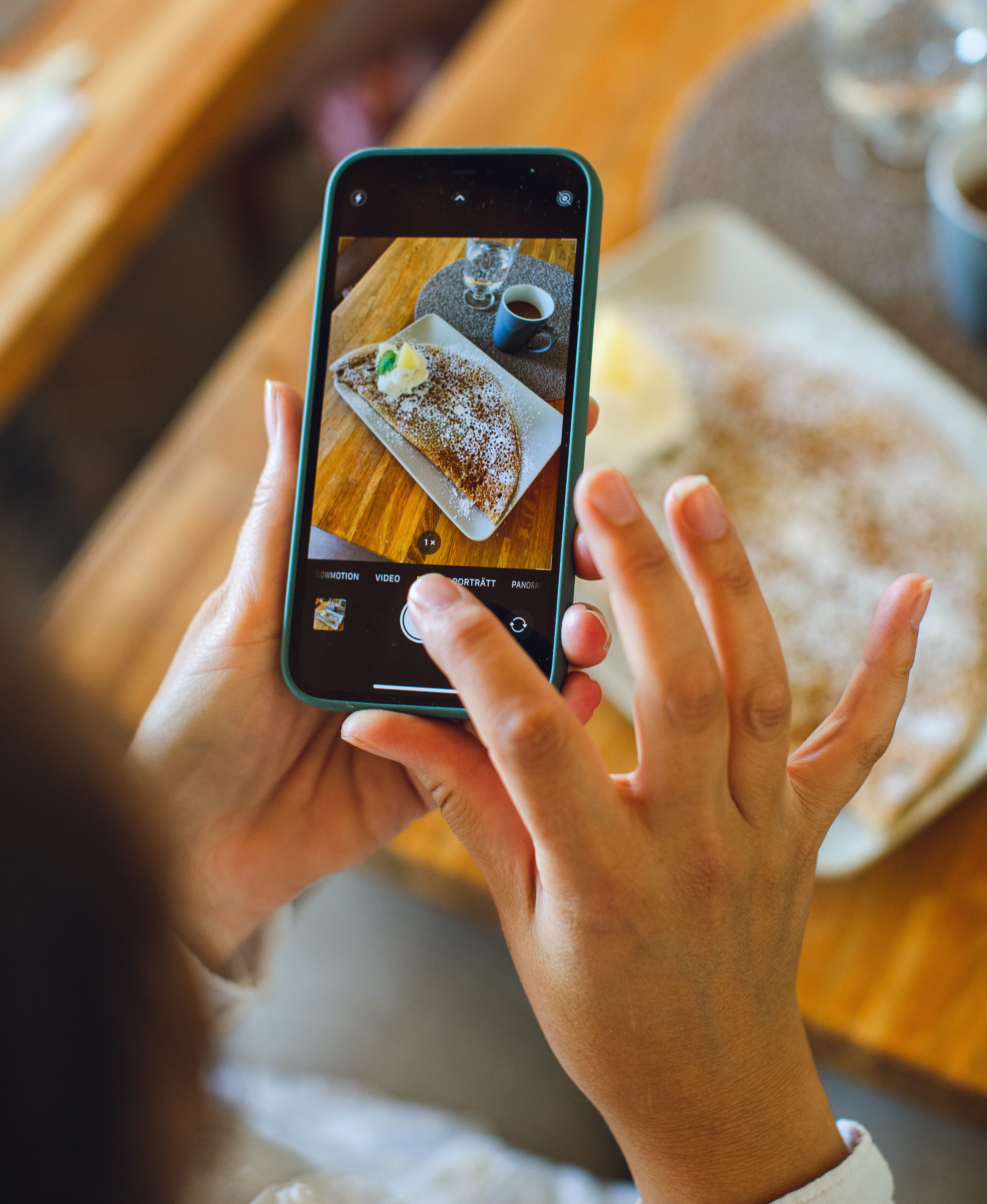 En person tar en bild med en smartphone. I telefonen syns bilden som är på en galette och en kopp kaffe. 