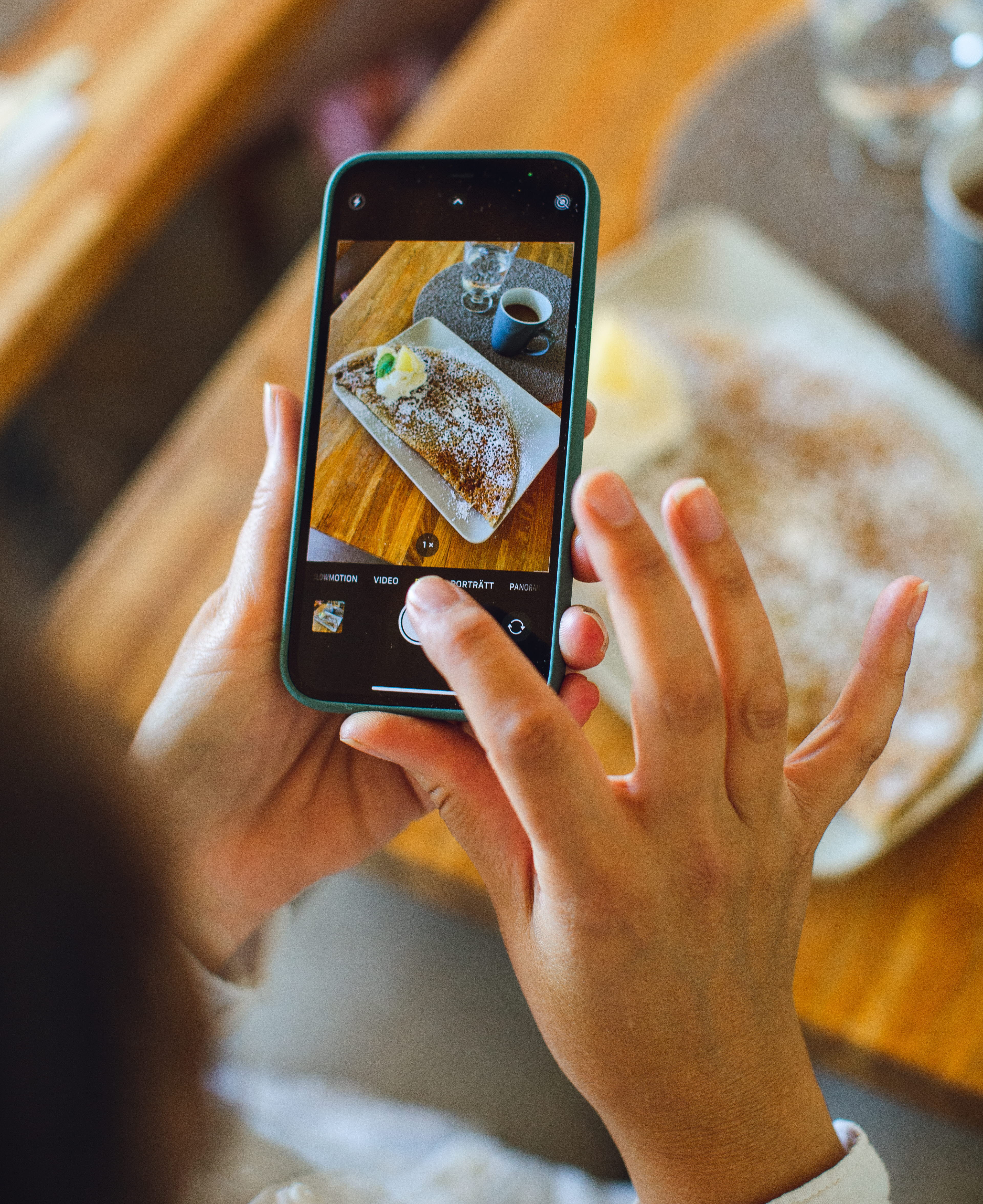 A person is taking a picture with a smartphone. In the phone you can see the picture which is a picture of a crêpe and a cup of coffee.