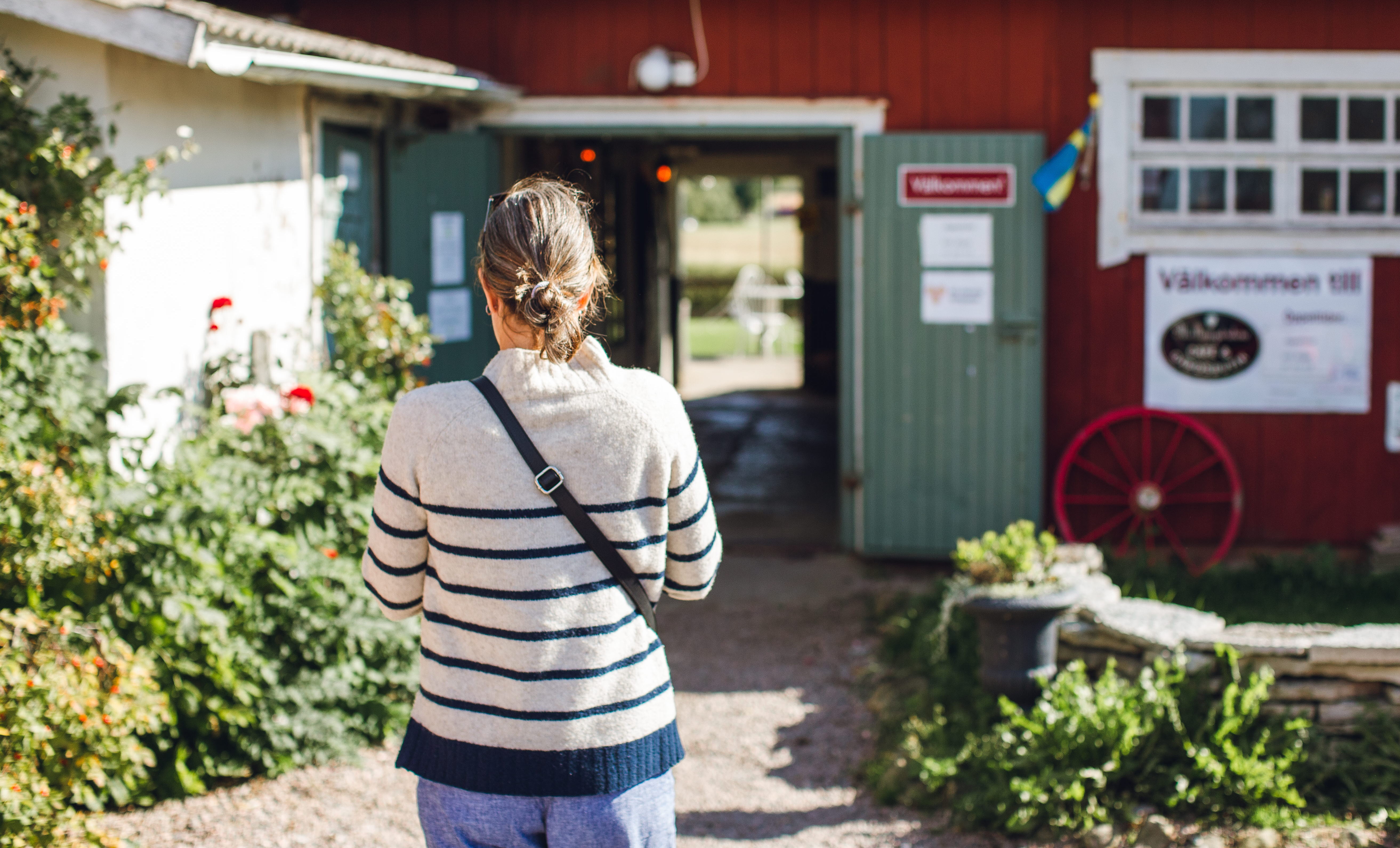 En person med randig tröja går mot en gammaldags röd ladugårdsbyggnad. 