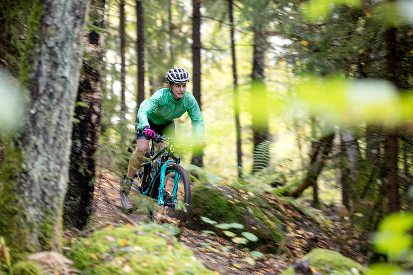 En kvinna i turkosa kläder på turkos mountainbike cyklar i skogen en solig höstdag.
