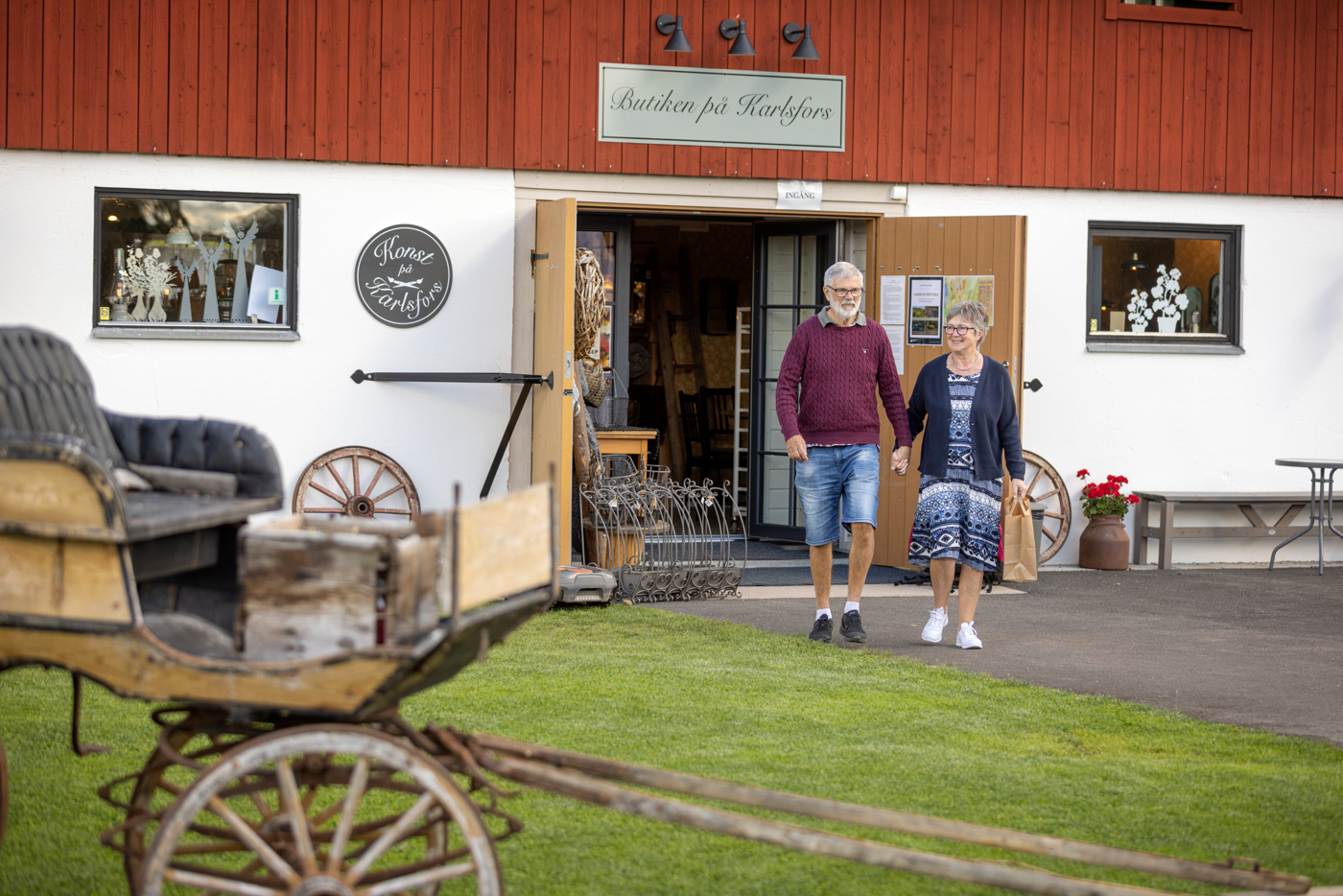 Ett äldre par går hand i hand ut från en inredningsbutik i lantlig miljö. 