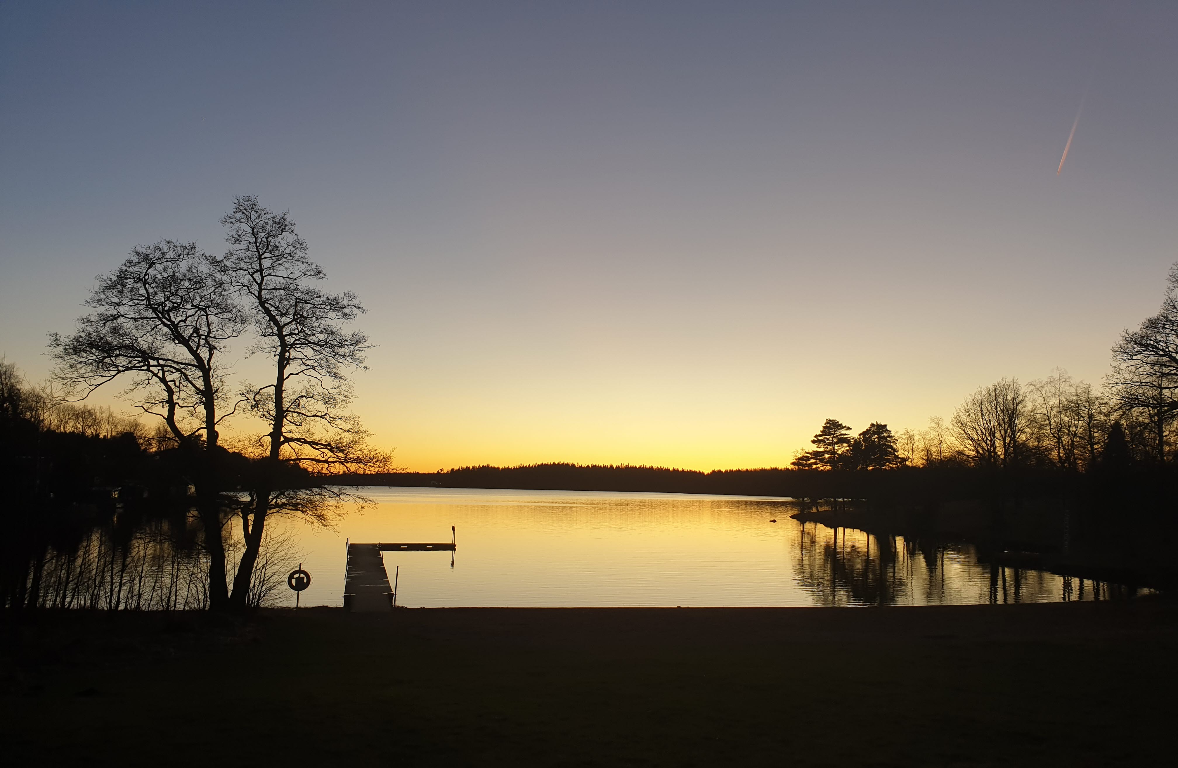 Solnedgång en vårkväll över en badplats med brygga.