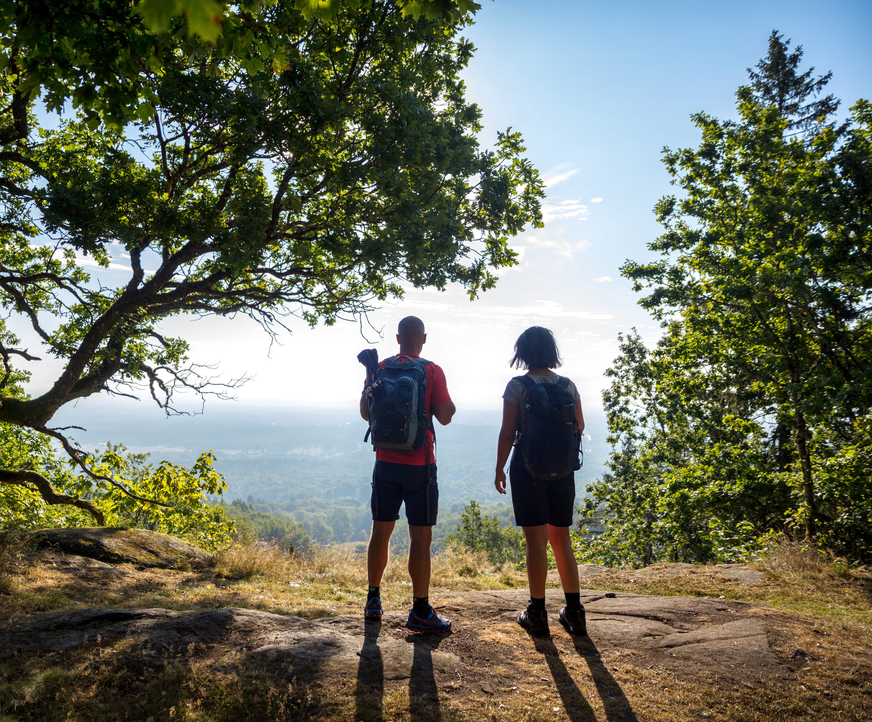 Two people stand on the edge of a mountain looking out over a magnificent landscape