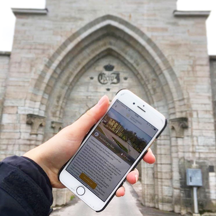 Hand som håller i en mobiltelefon som visar Karlsborgs fästnings appen 