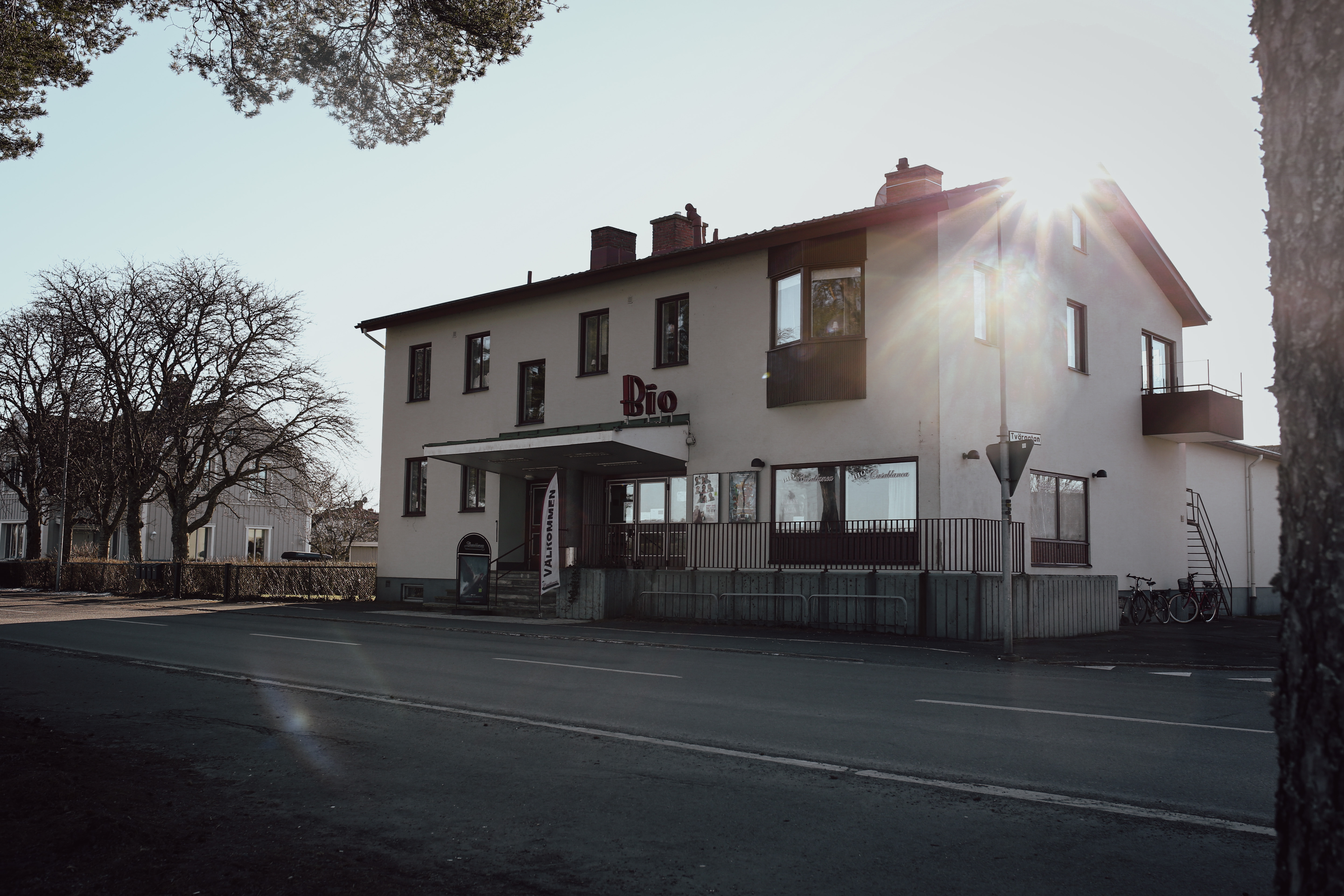 Ljust flerbostadshus med en biograf i nedre plan. Starkt solsken mot kameran som bildar solkatter.