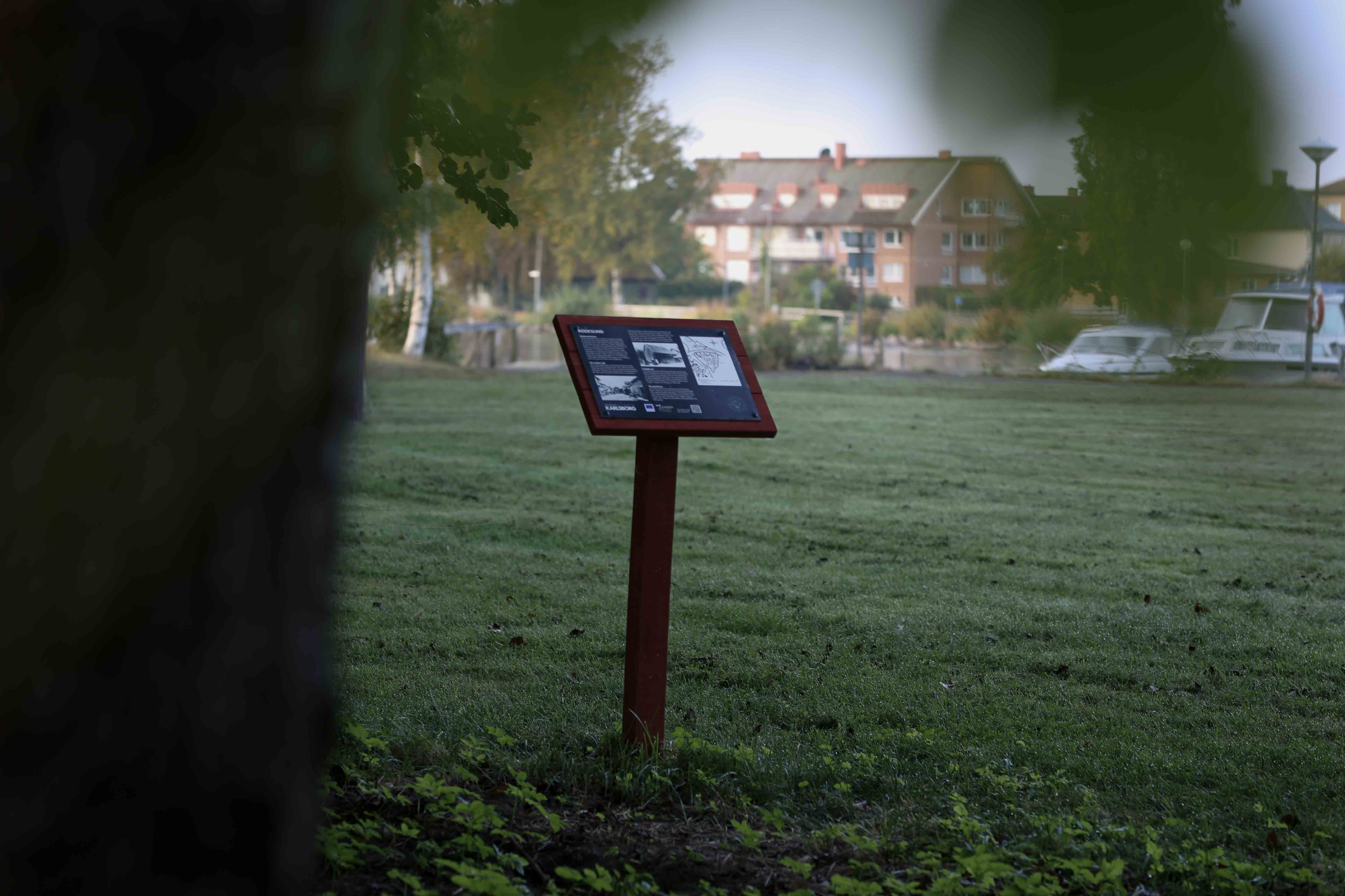 A red-painted sign holder with a mounted information sign. The information sign contains white text on a black background.