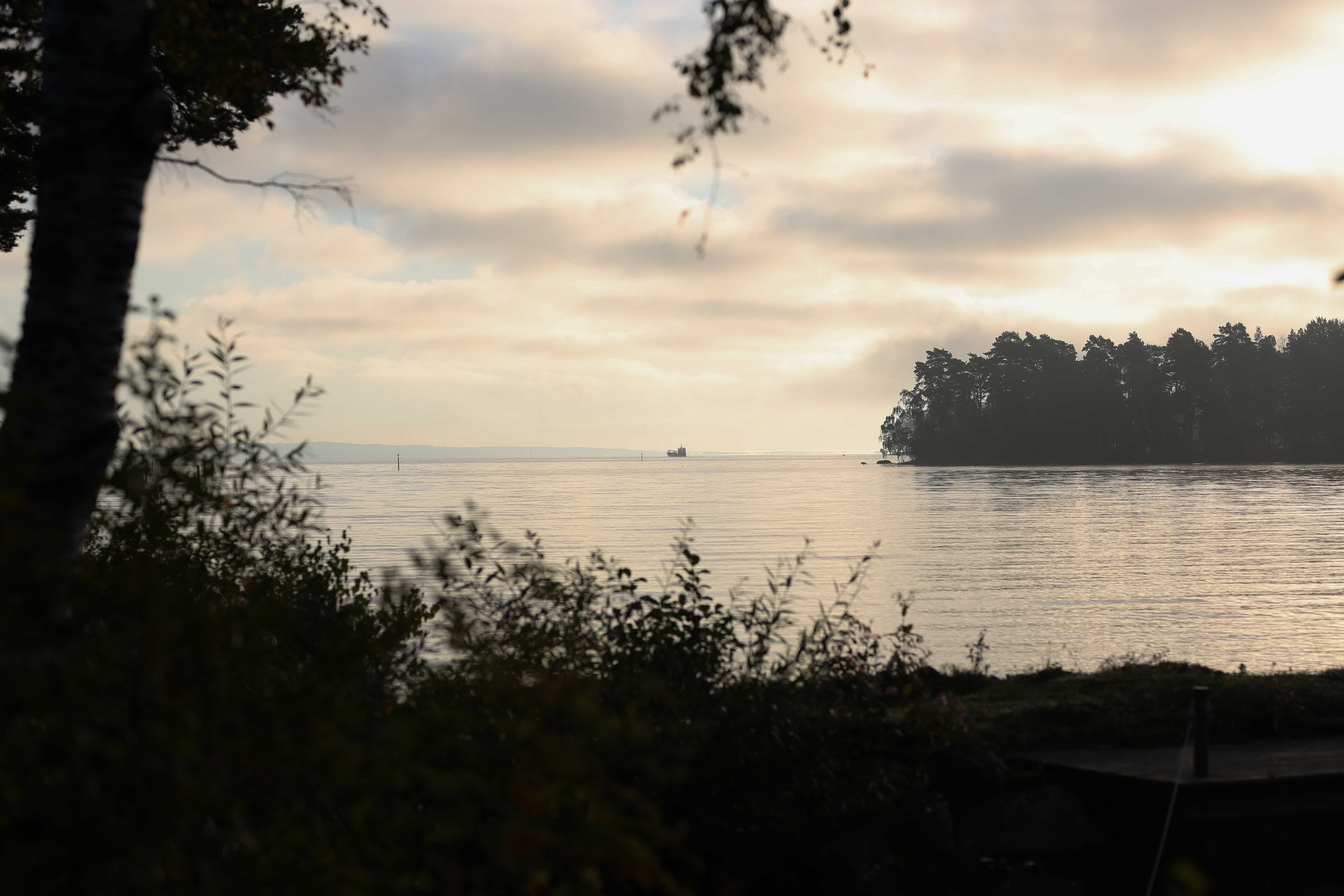 Morgonljus över Vättern. En ö bryter horisontlinjen till höger i bild och ångt bort i horisonten skymtar en båt. 