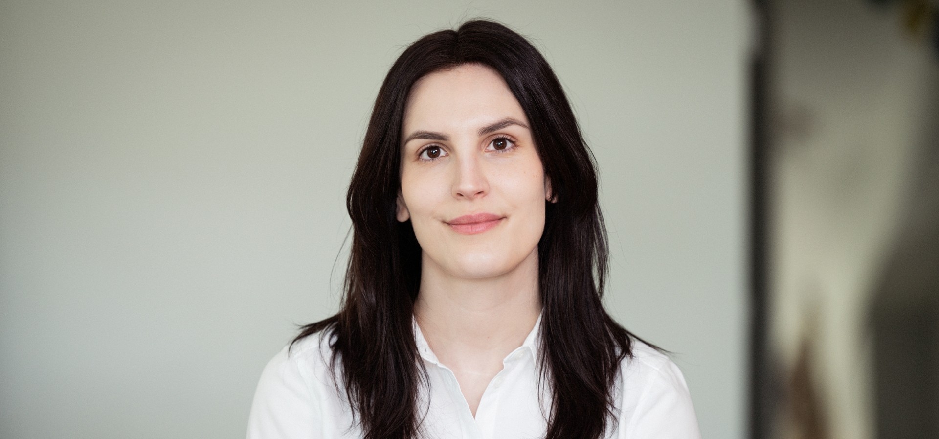 Person med mörkt långt hår tittar leende in i kameran