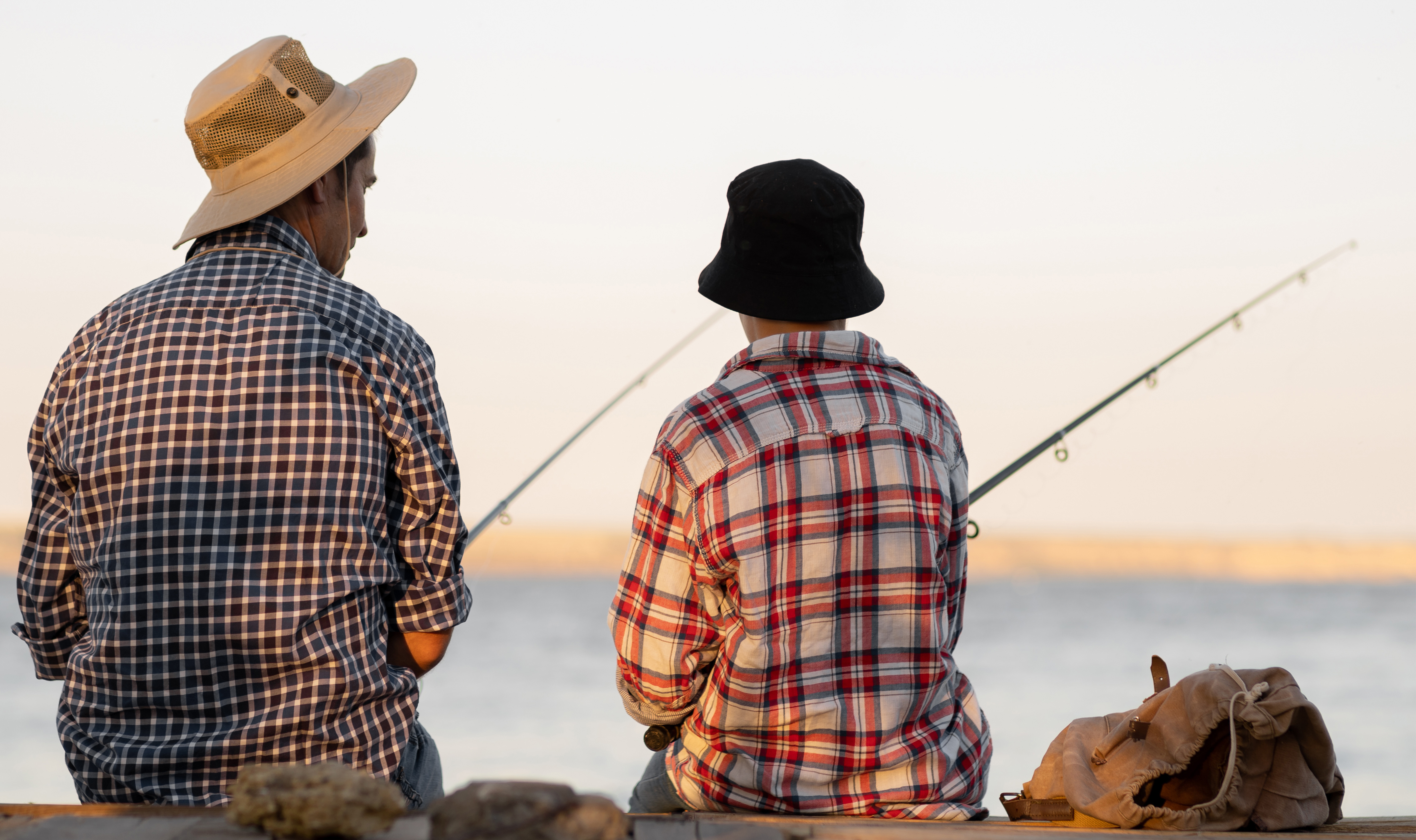 En vuxen och ett barn i fiskehattar sitter och metar tillsammans