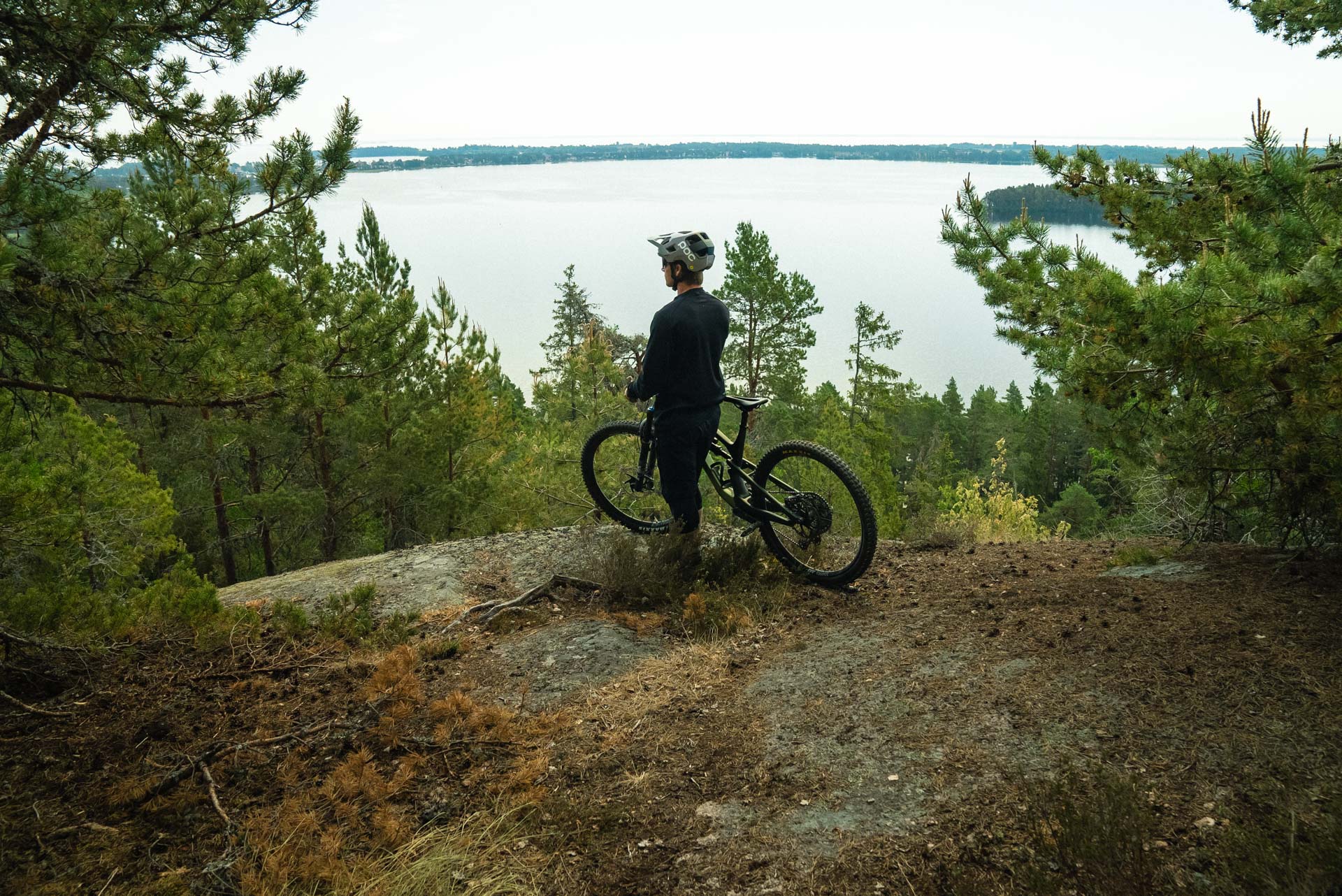 Man med cykel på en berghäll med utsikt över en sjö.