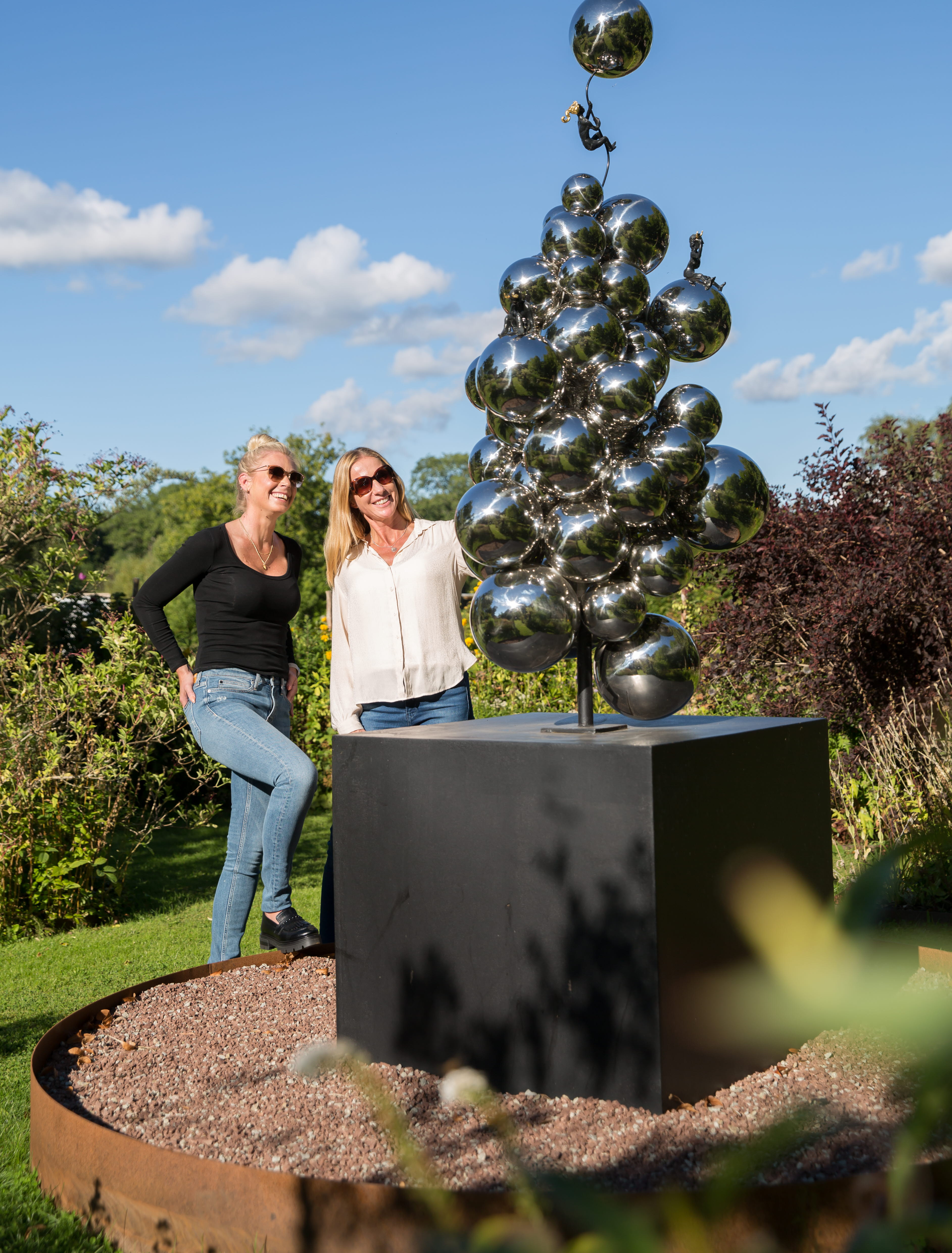 Två kvinnor står och kollar på en skulptur i en trädgård.