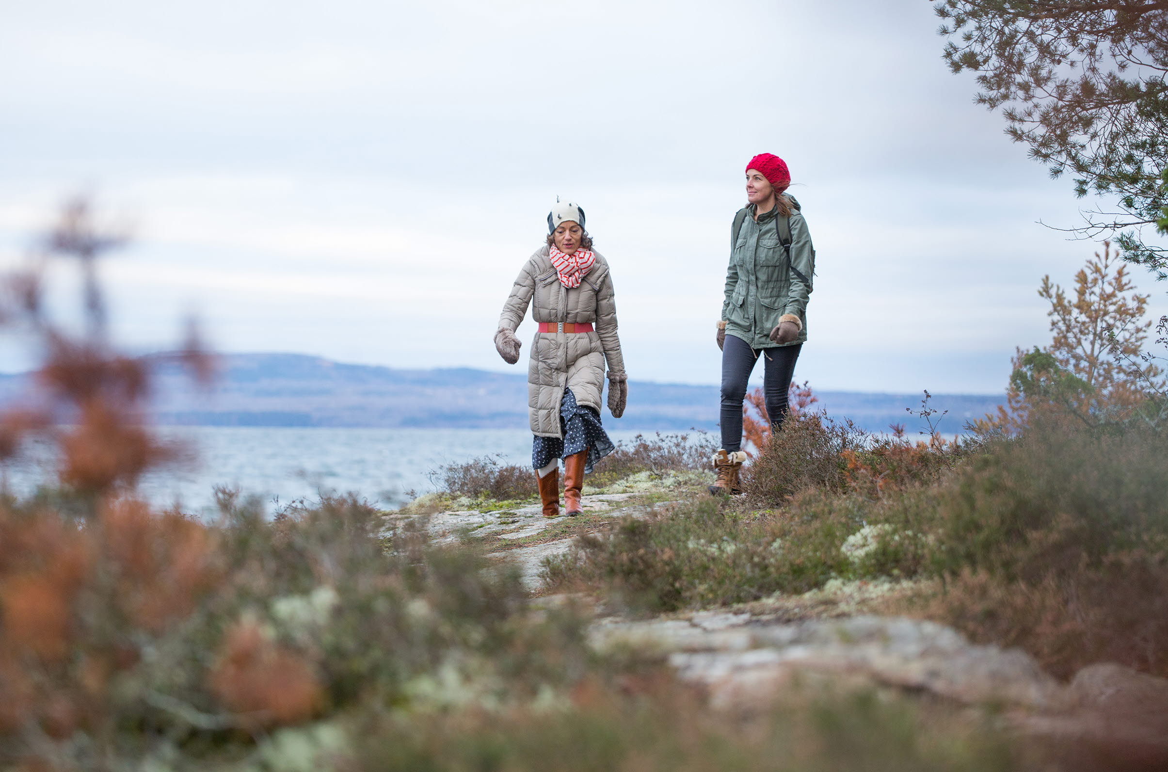 Två kvinnor vandrar i naturen på vintern. Berget Kinnekulle och sjön Vänern syns bakom dem.