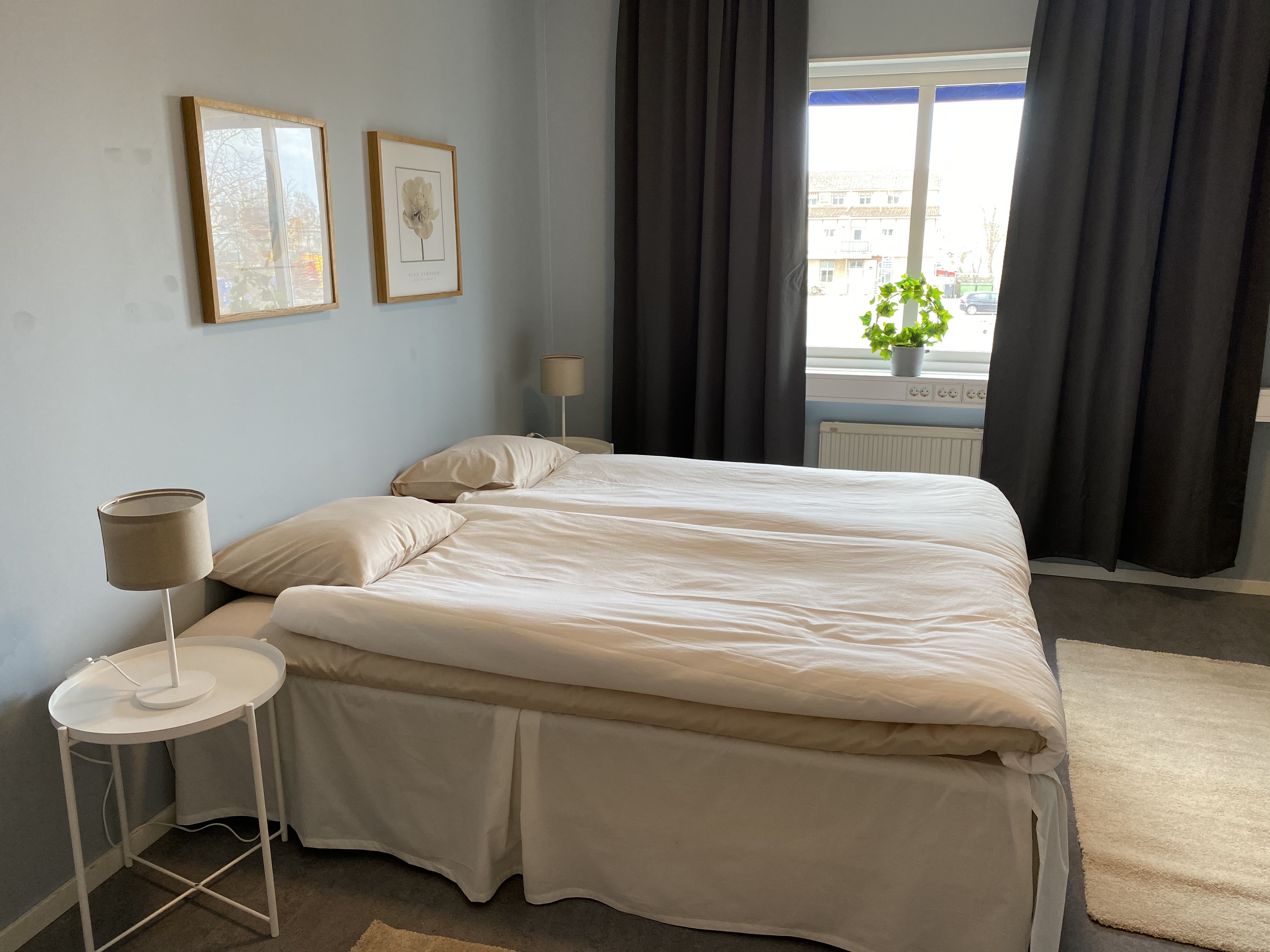 En dubbelsäng med nattduksbord och två tavlor över sängen.