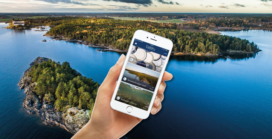 A hand holdin a smart phone in fron of a costal scenery