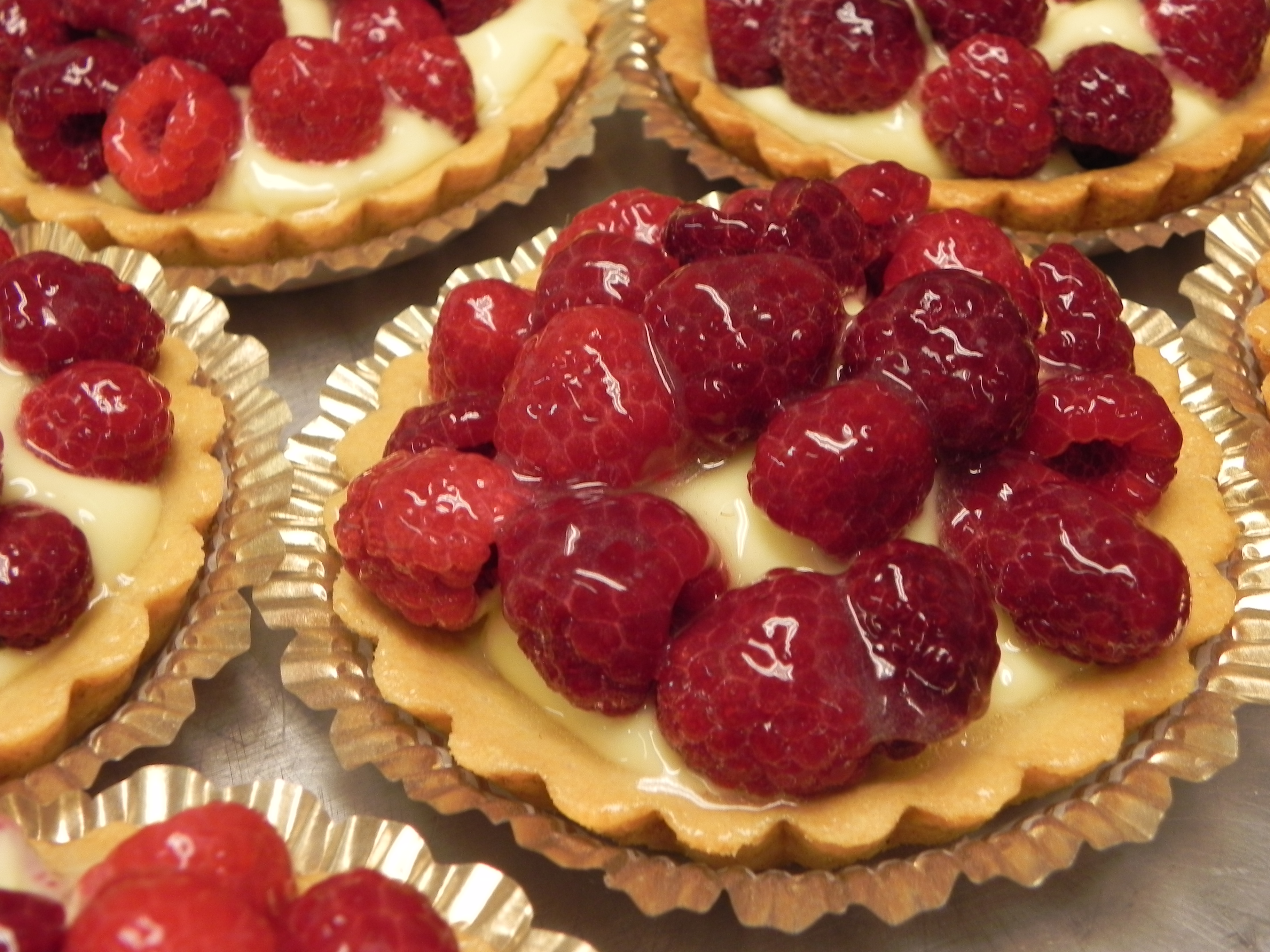 Närbild på kakor i aluminium formar. Kakorna är toppade med hallon.