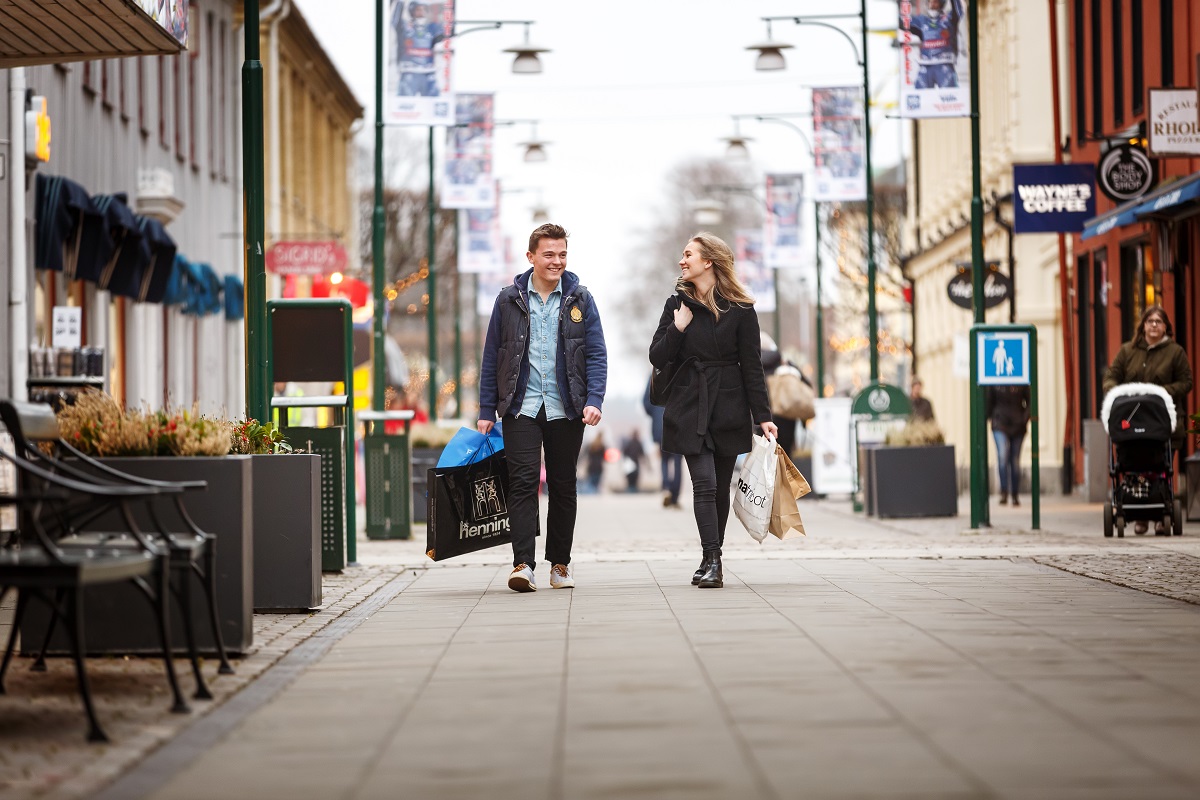 Ung man och kvinna promenerar i stadsmiljö med shoppingkassar i händerna. 