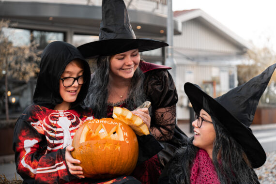 På bilden syns två barn och en kvinna utklädda till häxor  och skelett. De håller i en karvad pumpa
