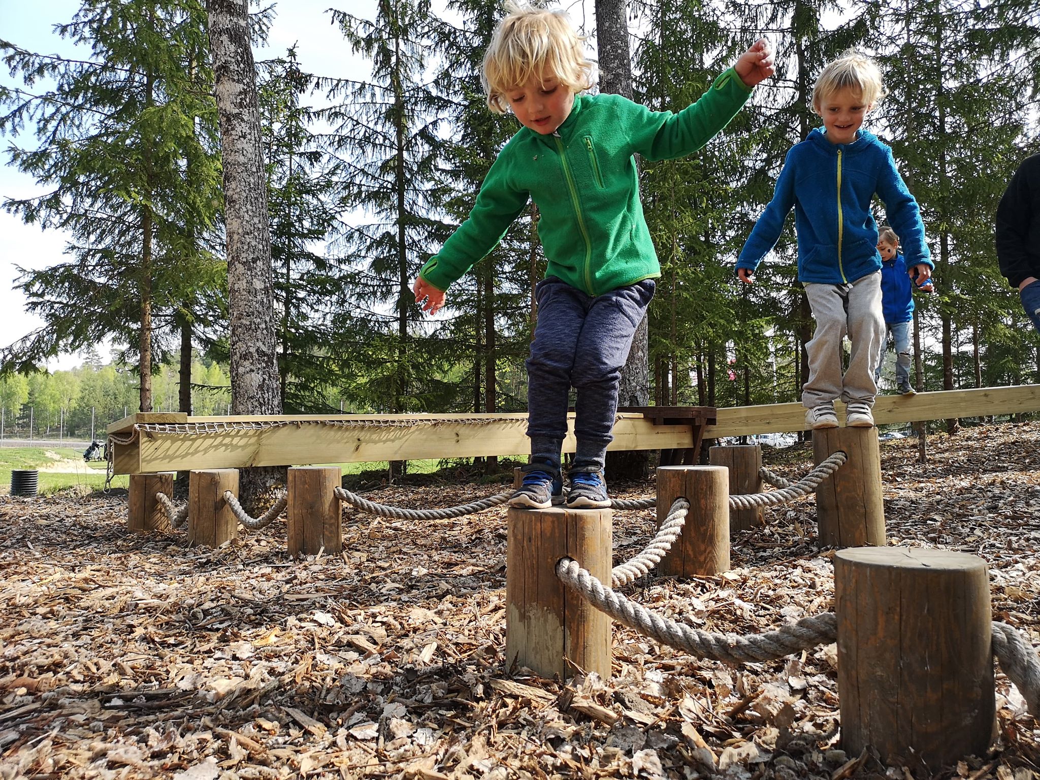 Two kids playing on an obstacle course in nature.