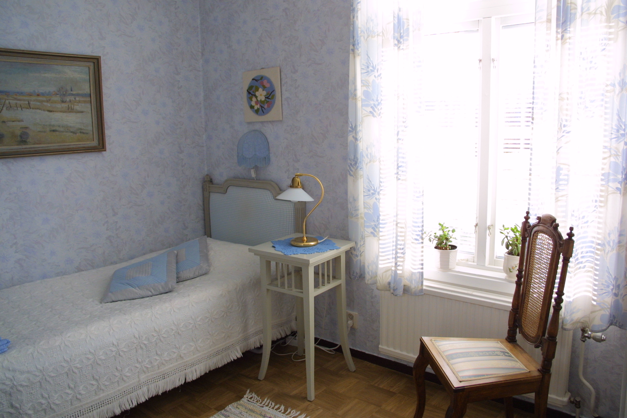 Ett blå rum med en enkel säng och en vit sängbord bredvid. 