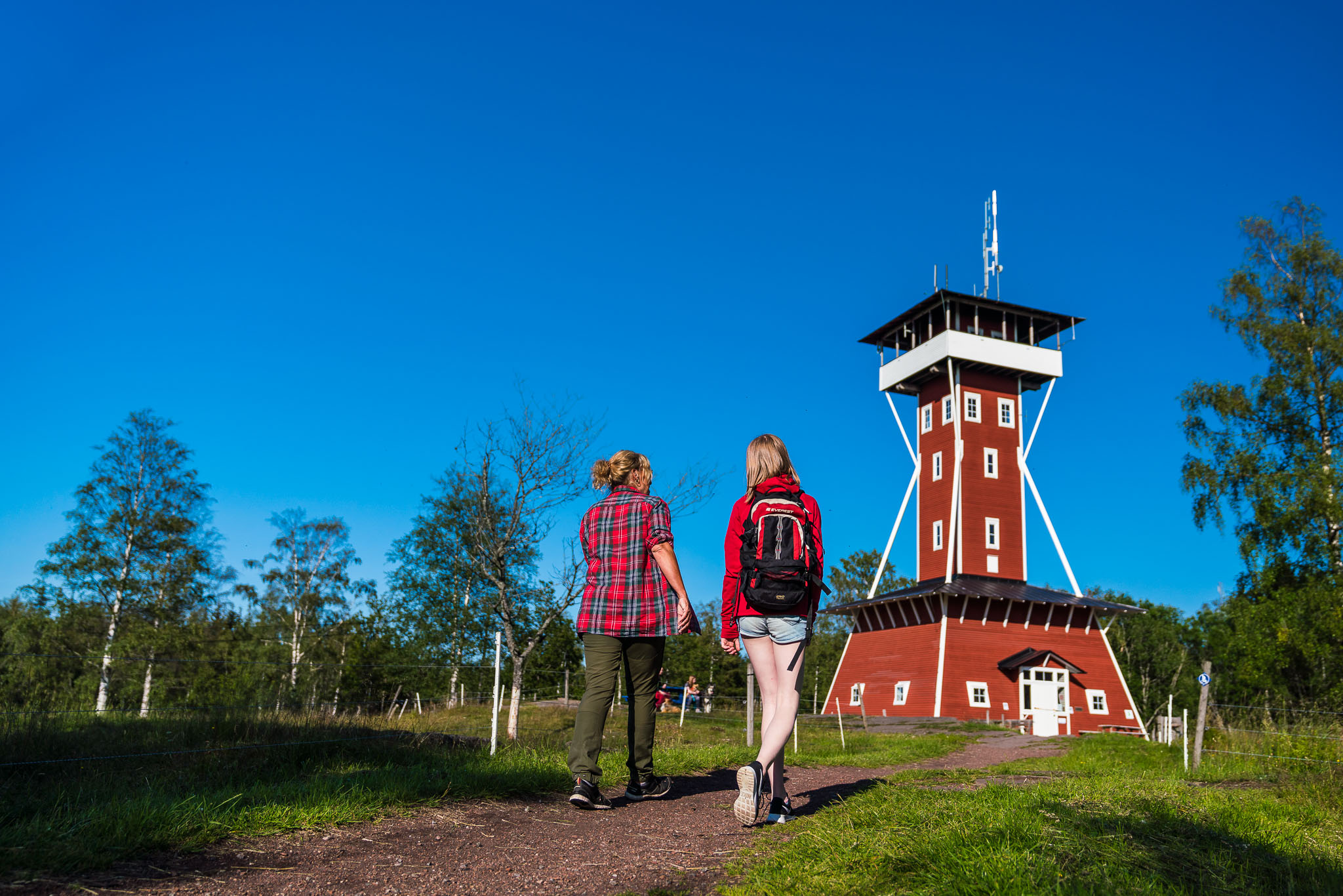 Two persons walking beneath a rd watch tower.