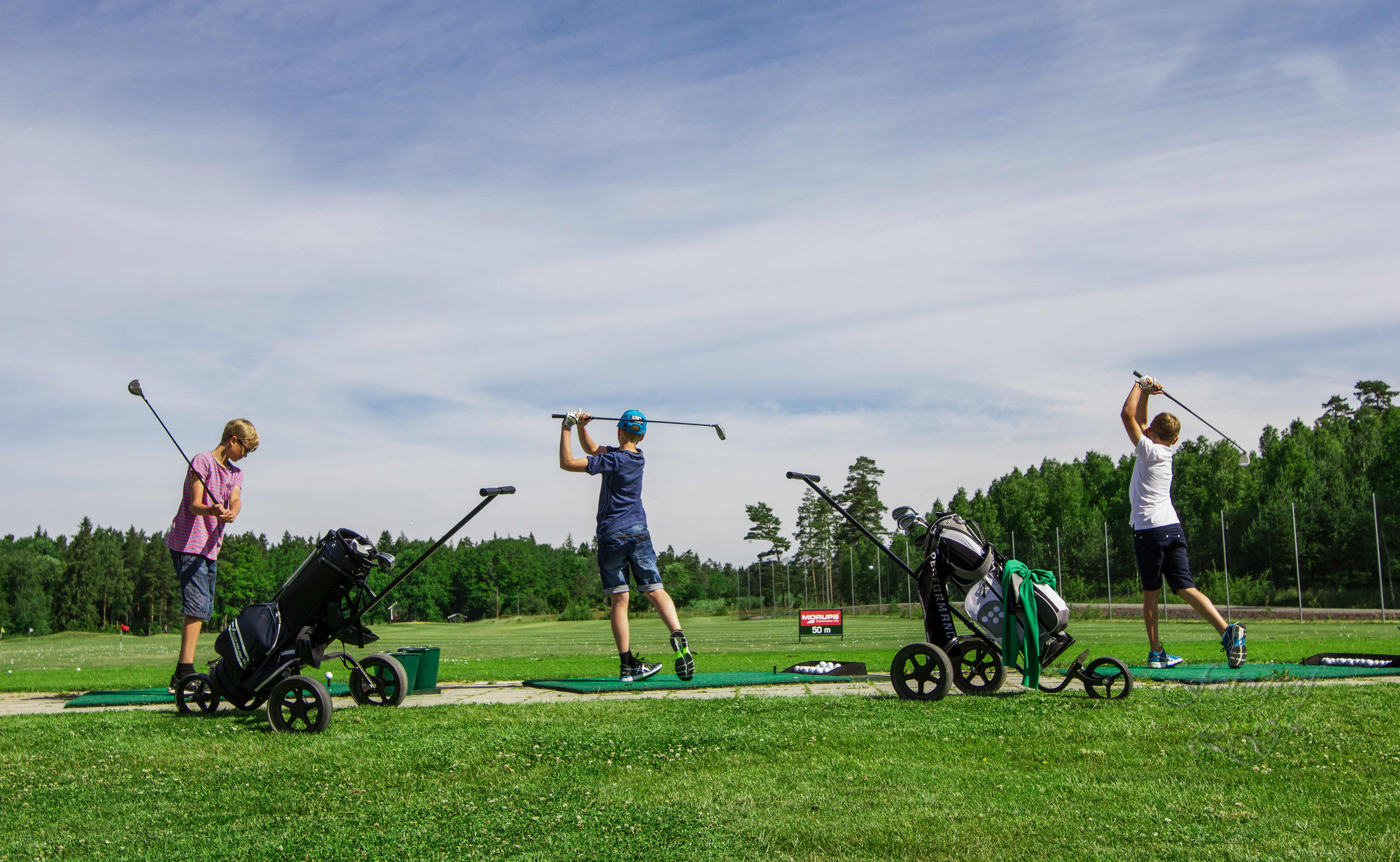 Några barn står och slår på en golfanläggning en solig sommardag. 