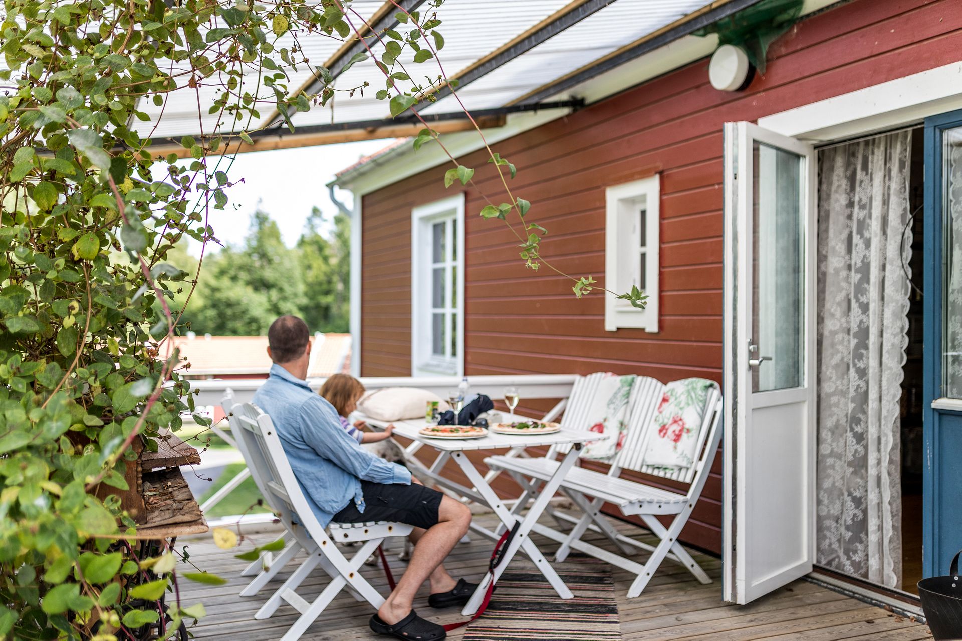 En man och ett barn sitter på en veranda utanför ett rött hus