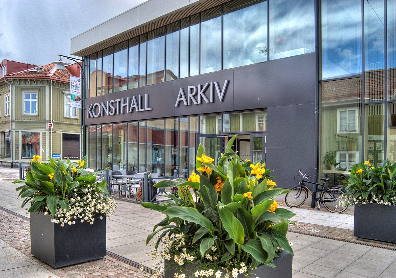 En gatuvy där man ser en byggnad med skyltar där det står "konsthall" och "arkiv".