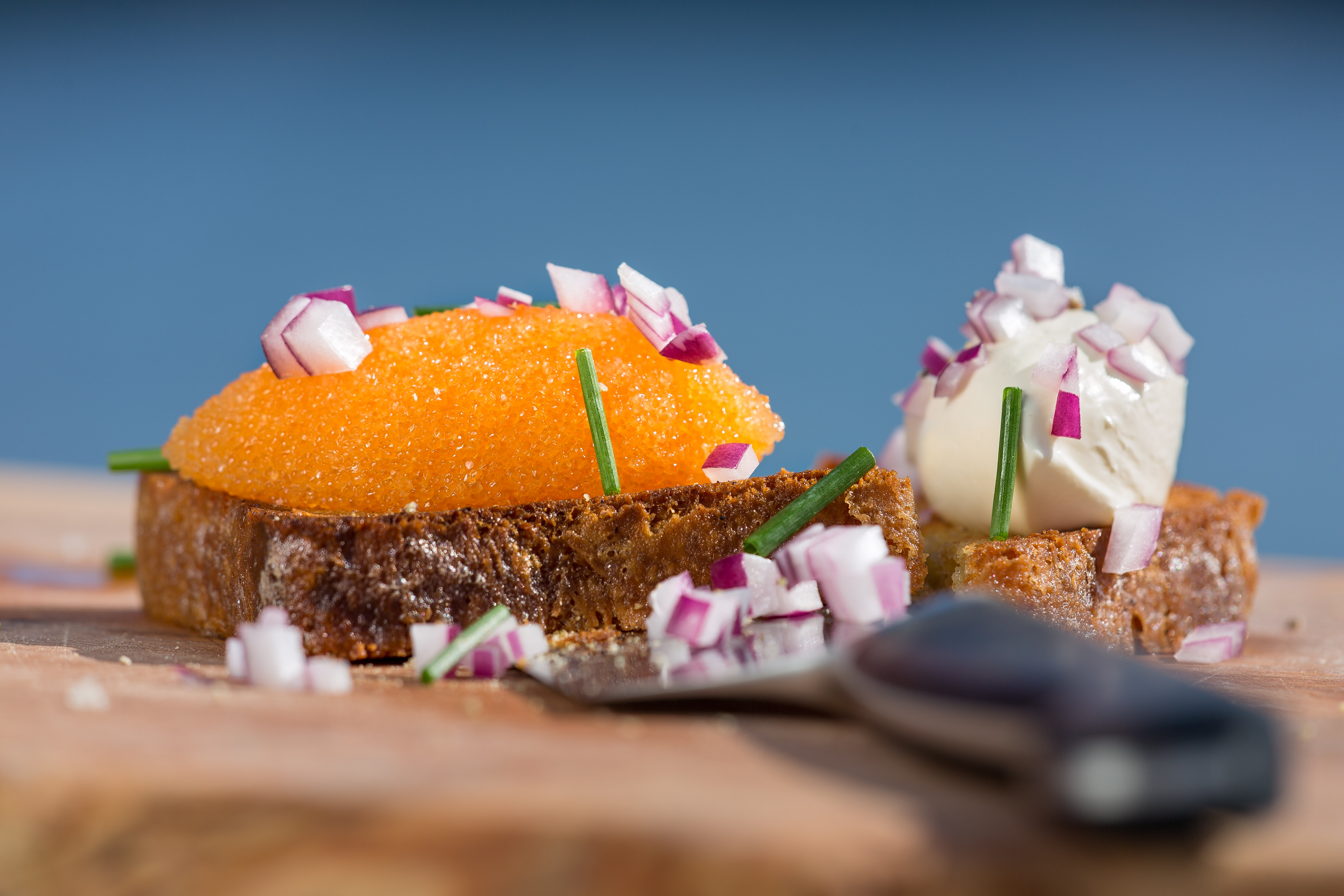 Brödskiva full av löjrom och finhackad rödlök. I förgrunden ligger en kniv.