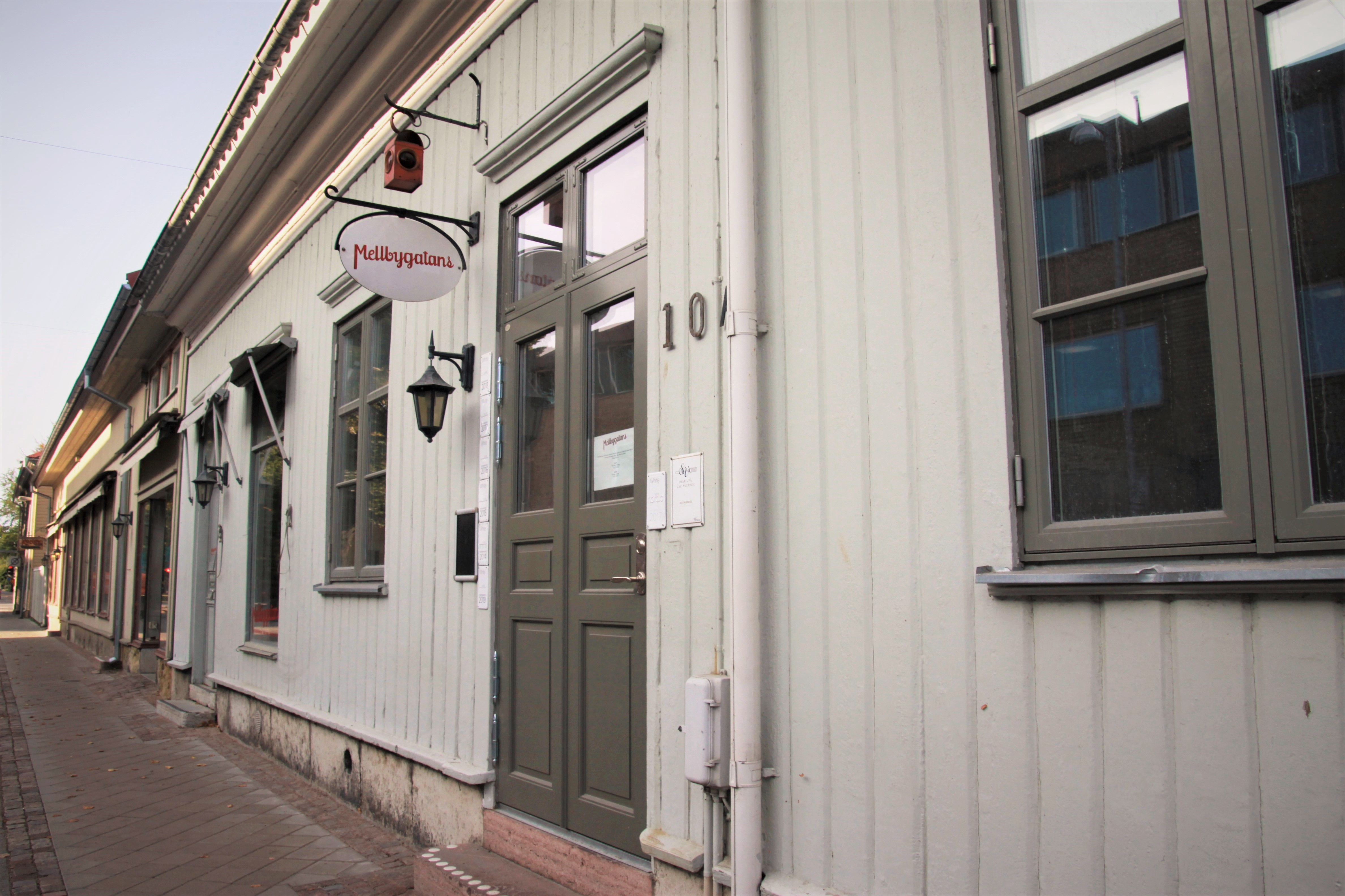 Ljusgrönt äldre trähus med mörkgröna detaljer kring dörr och fönster. Över dörren hänger en skylt med texten "Mellbygatans" och talet 10 sitter på husväggen.