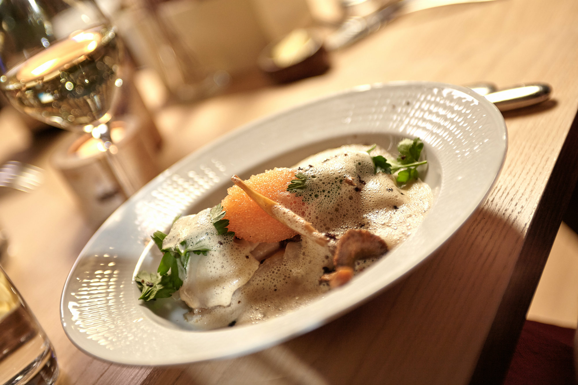 Tallrik med fint upplagd mat. Löjrom från Vänern och fisk. Bakom tallriken står ett glas vitt vin.