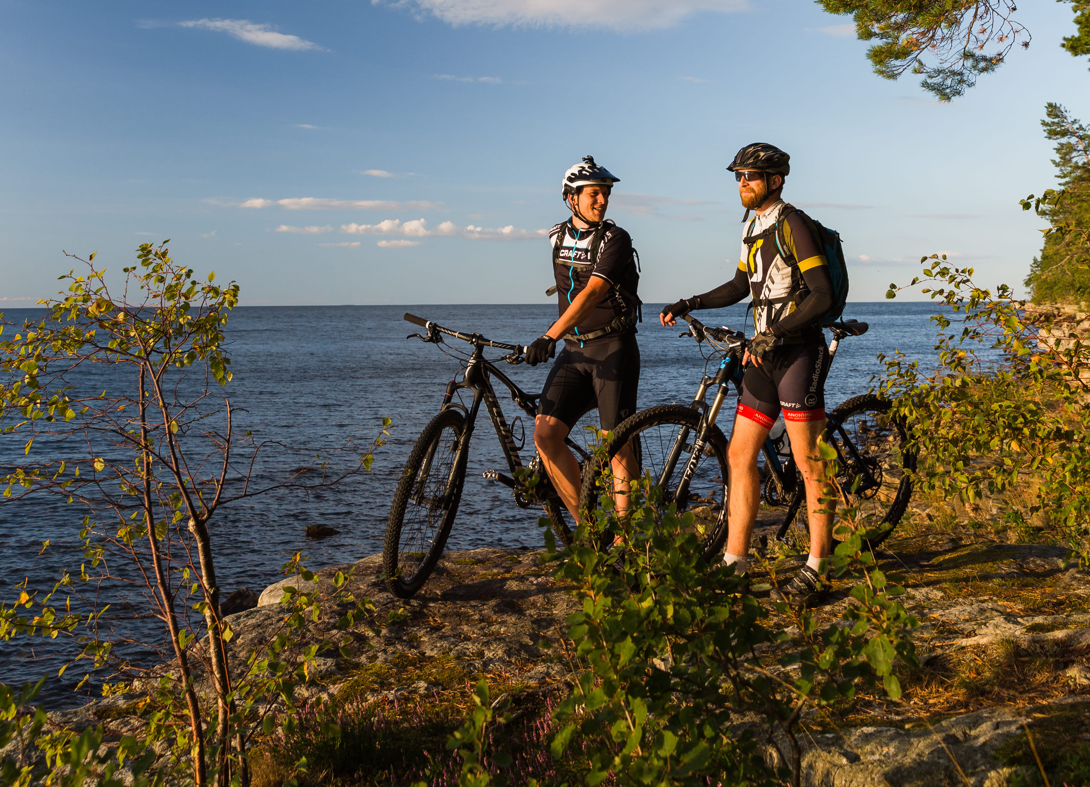 Två män tar en paus från sin MTB cykling och blickar ut över vattnet i kvällssolen.