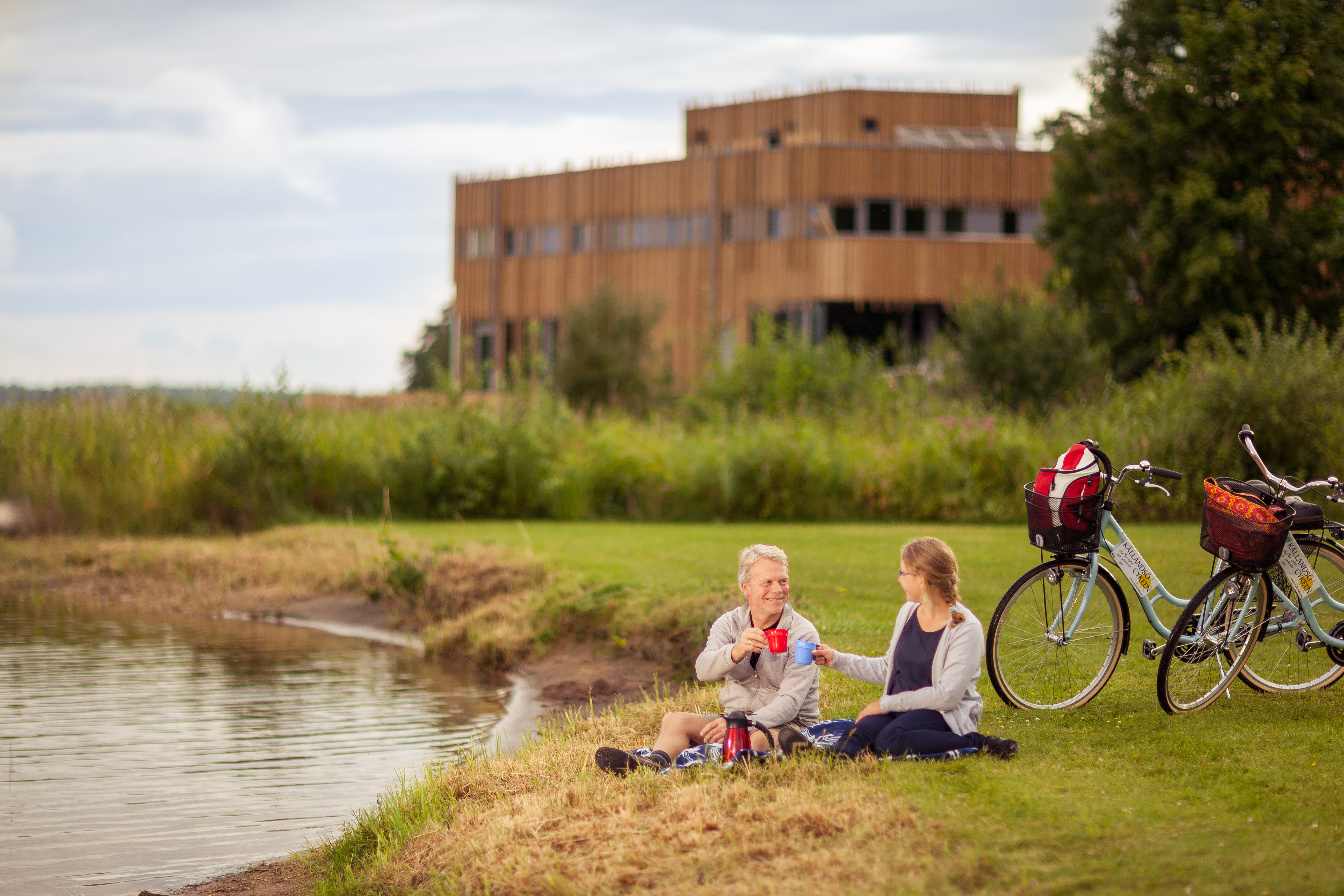 Två kvinnor med cyklar som sitter vid vattnet.