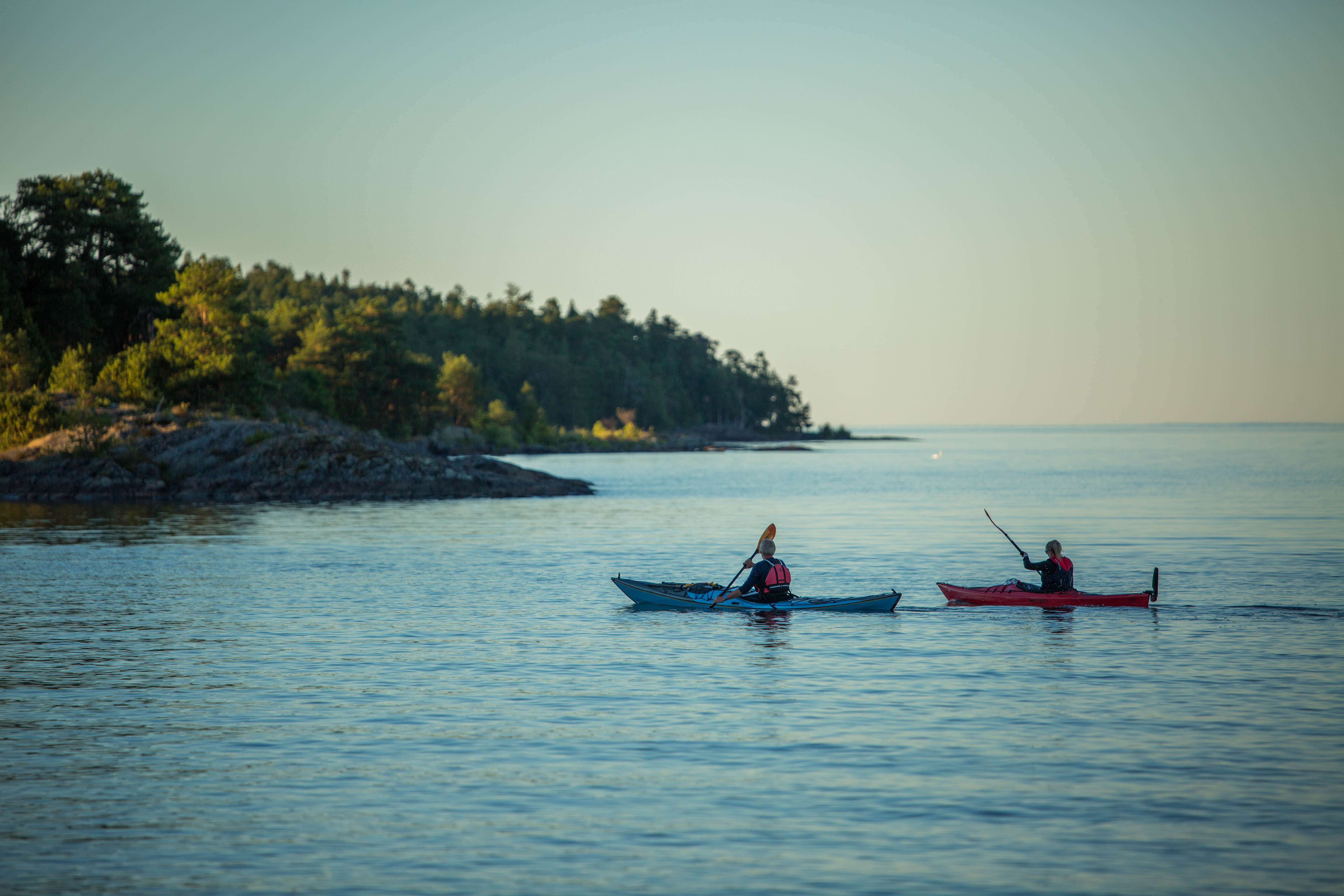 Två personer som paddlar kajak på stilla vatten en sommarkväll.