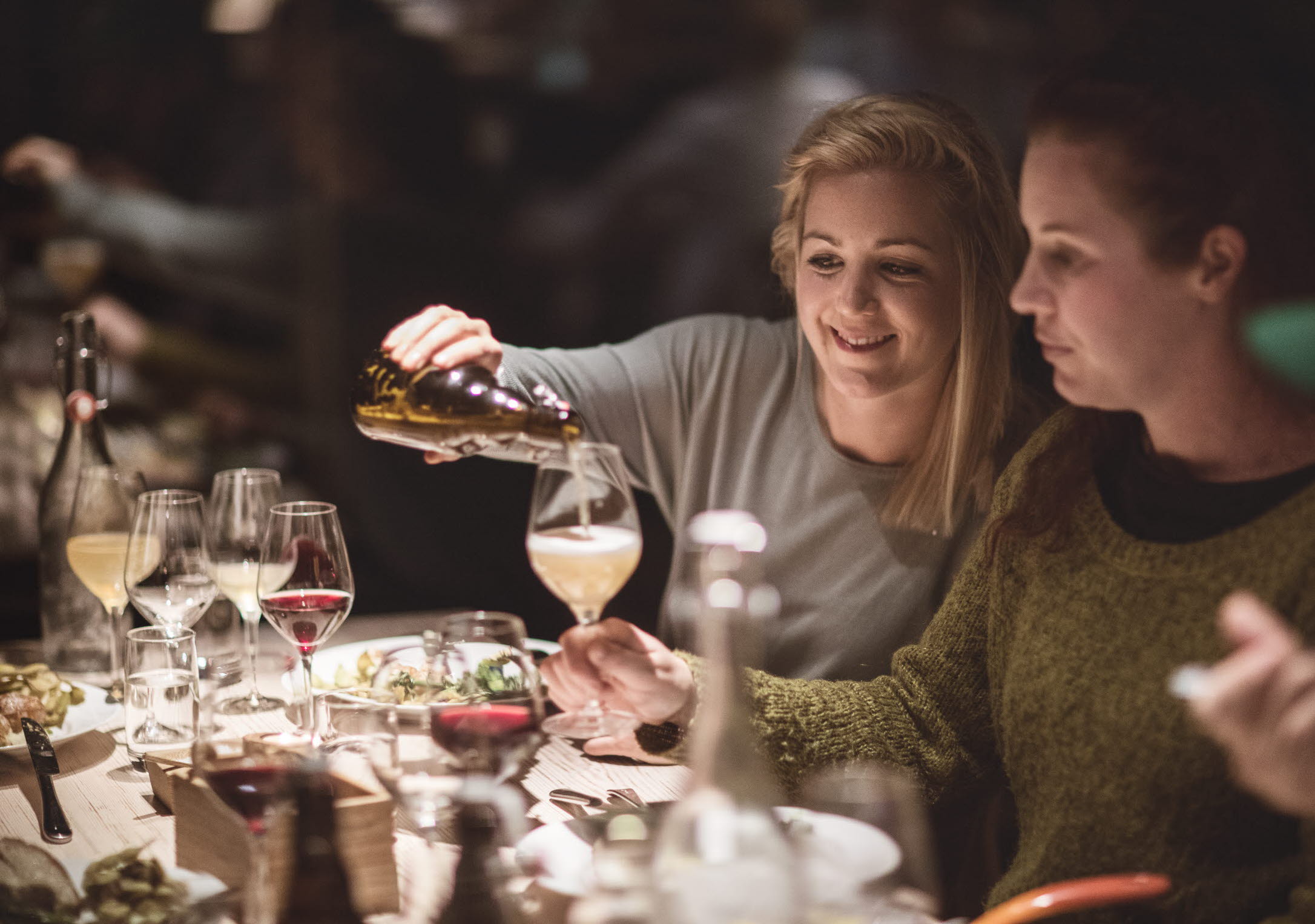Two women having dinner. One is pouring drinks to the other one.