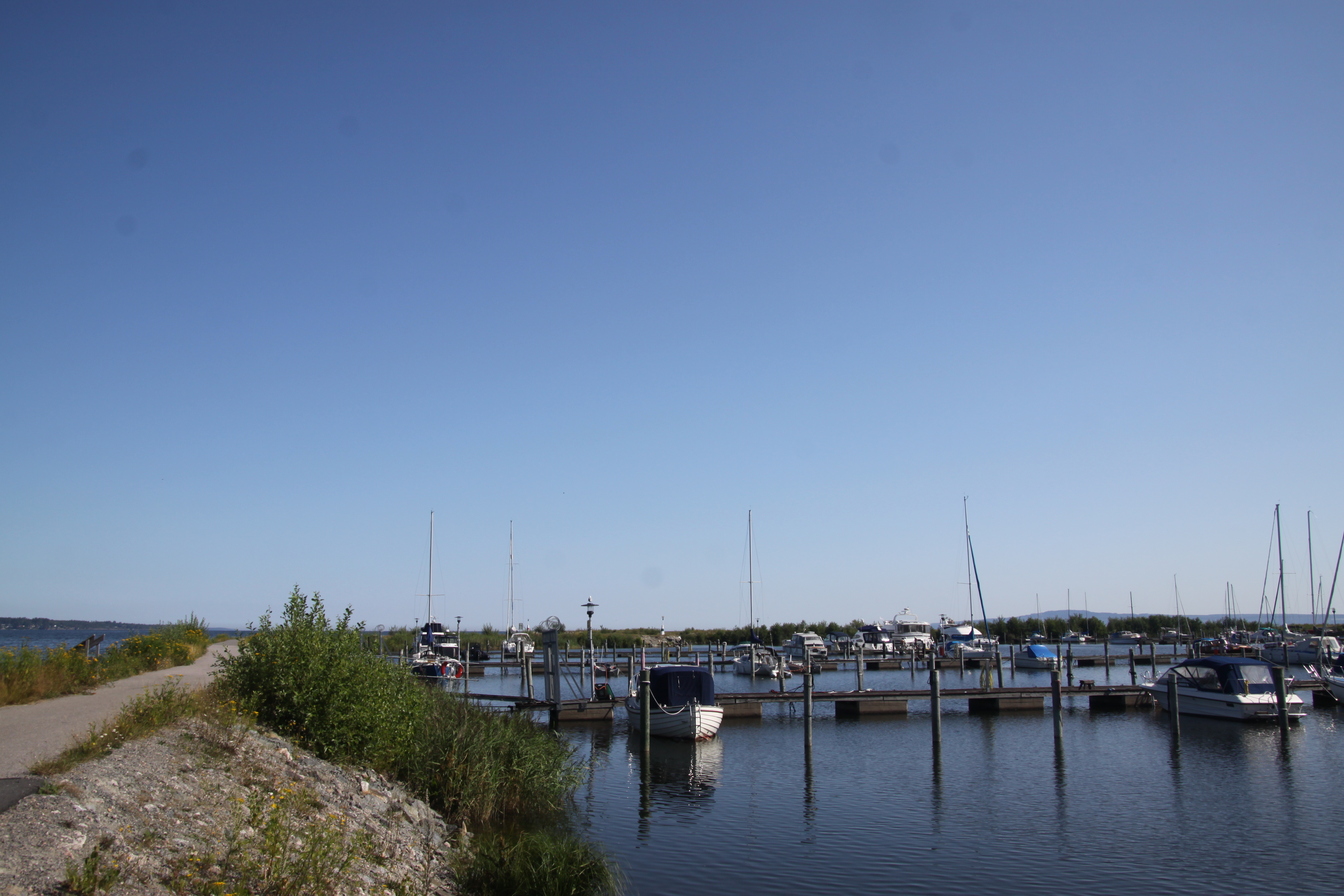 En vy över en stenpir ut i sjön med båtbryggor och enstaka båtar intillagda.