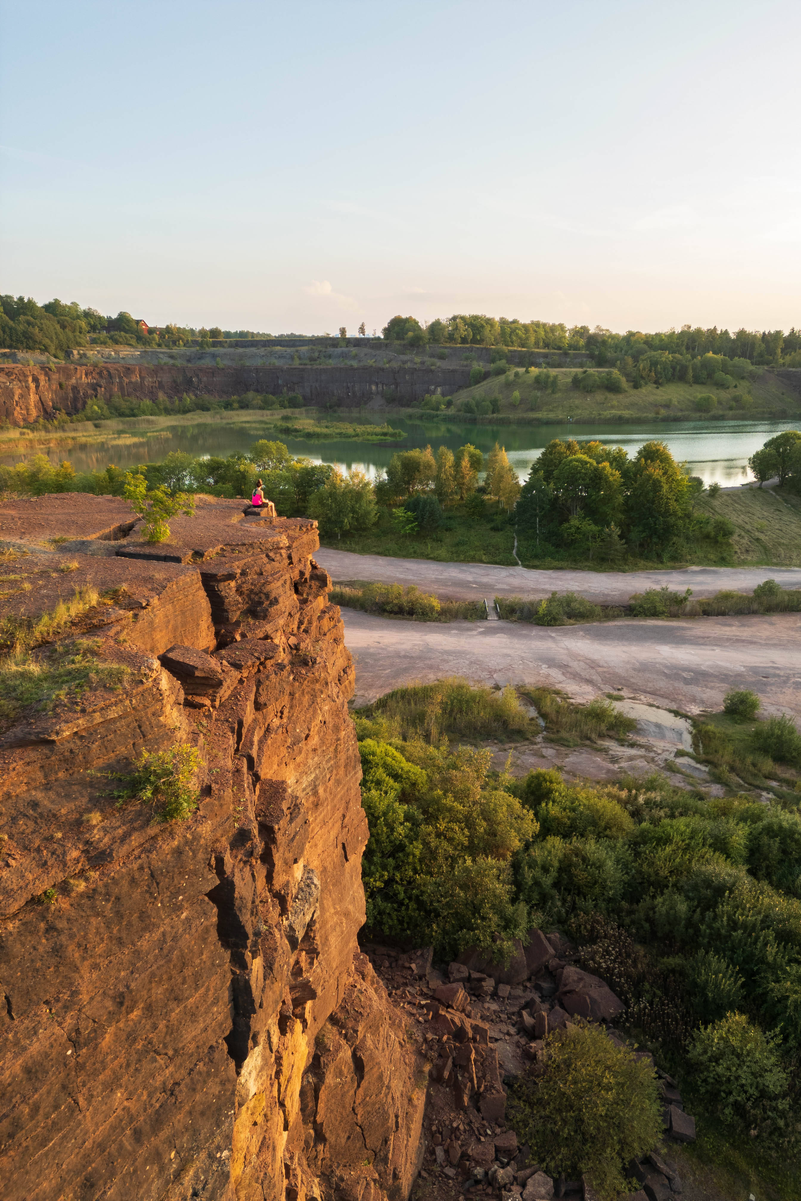 Kvinna sitter och blickar ut över stenbrott och damm i kvällsljus